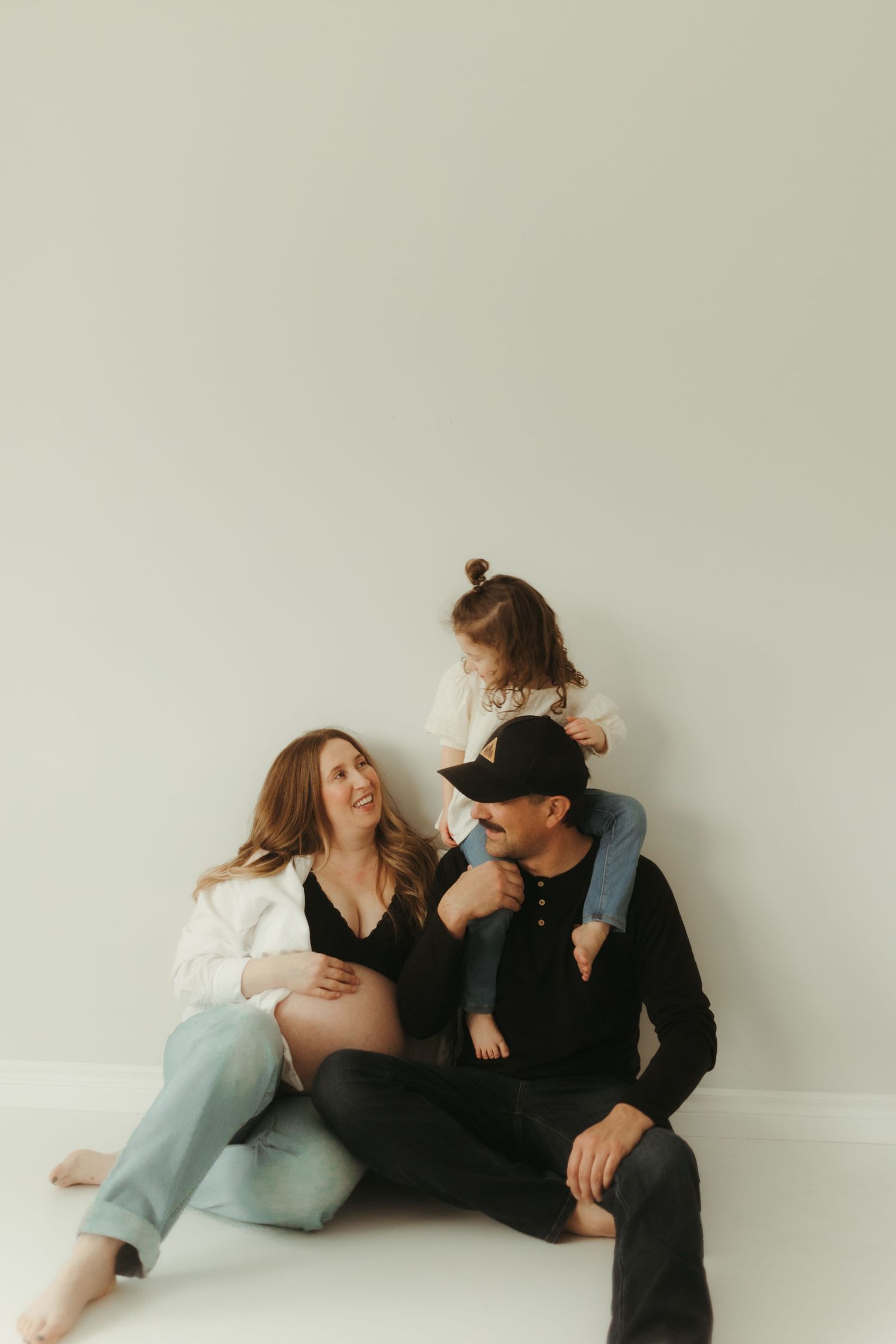 A family shares a tender moment together while sitting against a white wall.
