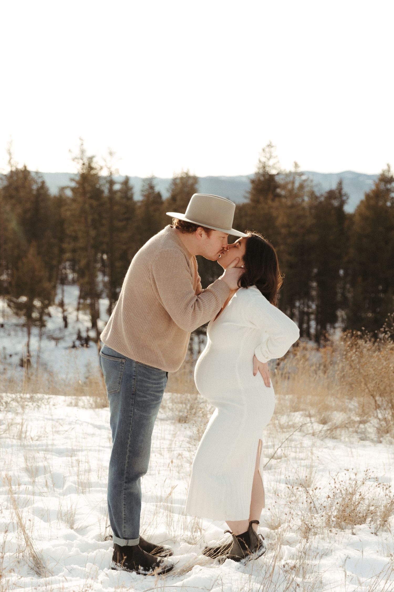 A couple shares a romantic moment in a snowy mountain landscape at sunset.