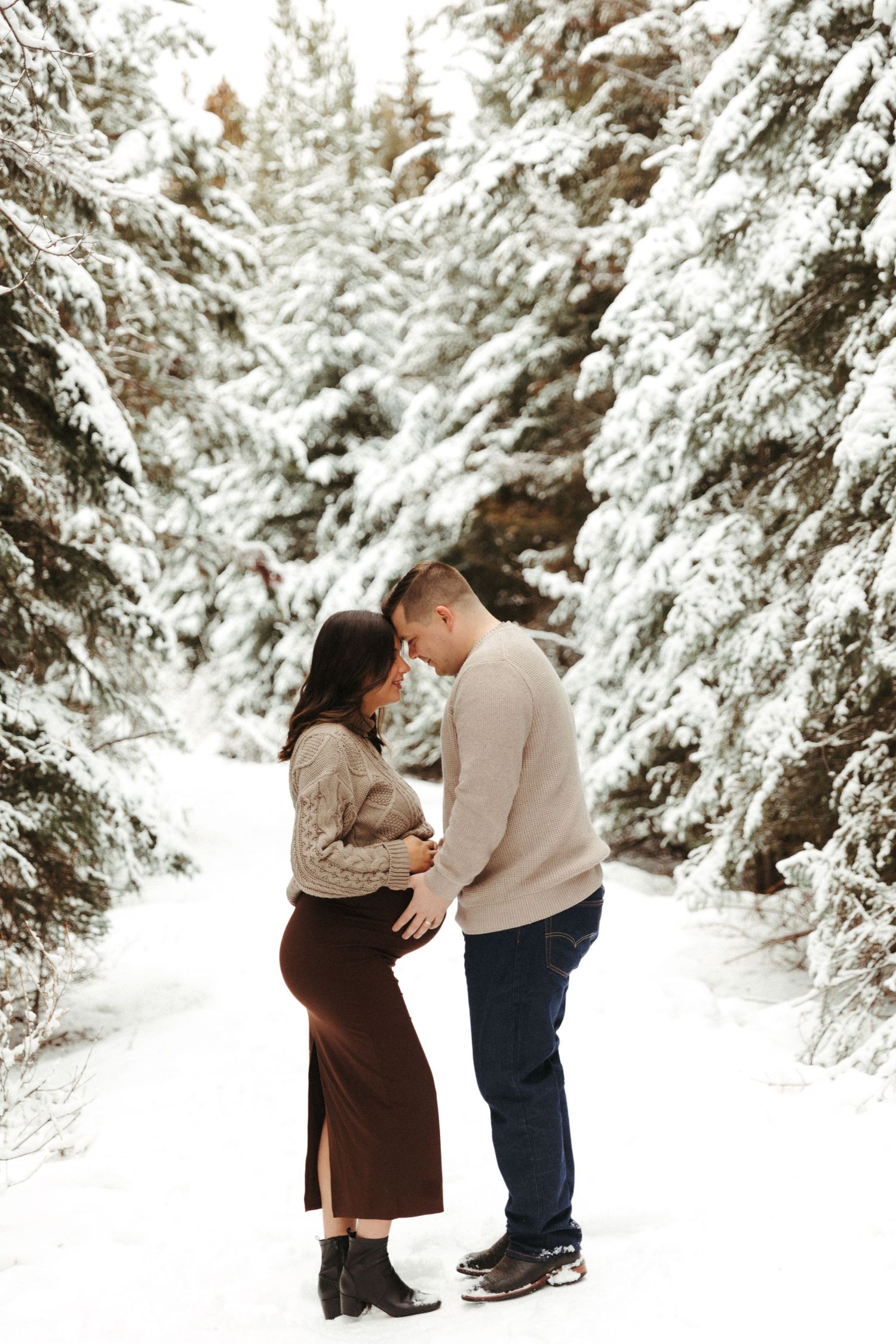 A couple shares an intimate moment in a snow-covered forest path.