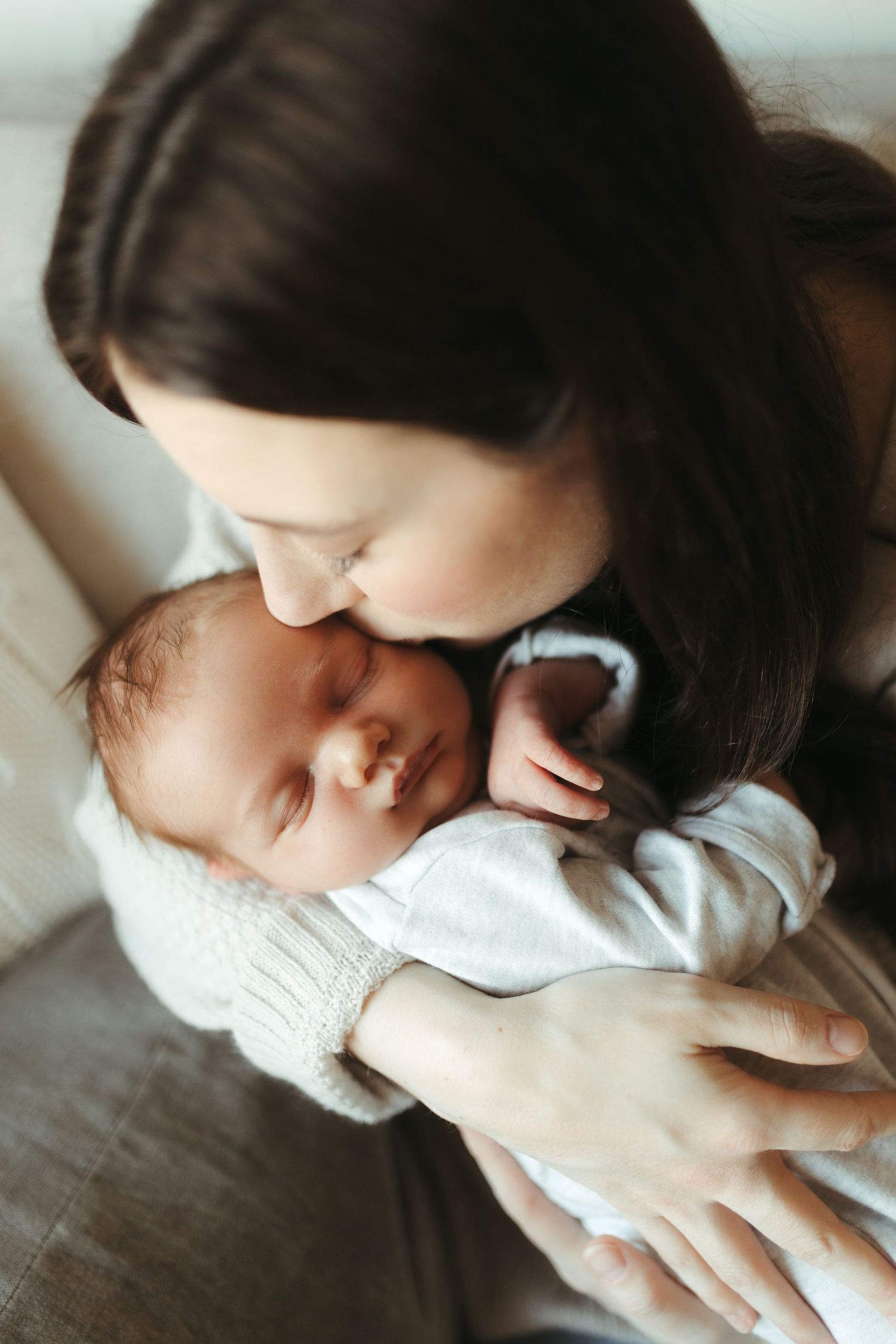 A tender moment between parent and newborn baby in soft window light.