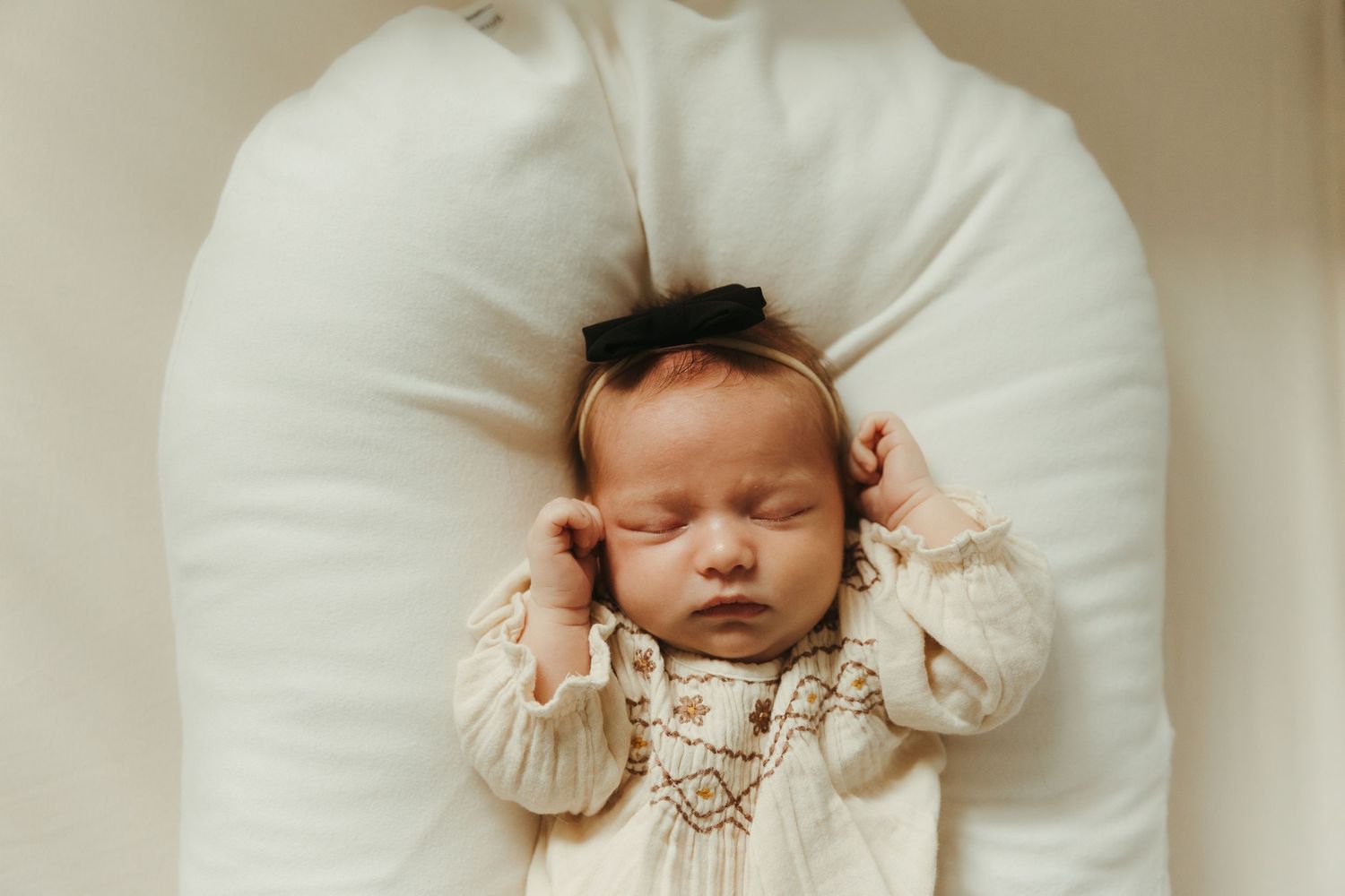 Sleeping baby in cream-colored ruffled outfit lying on white pillow in four similar poses.