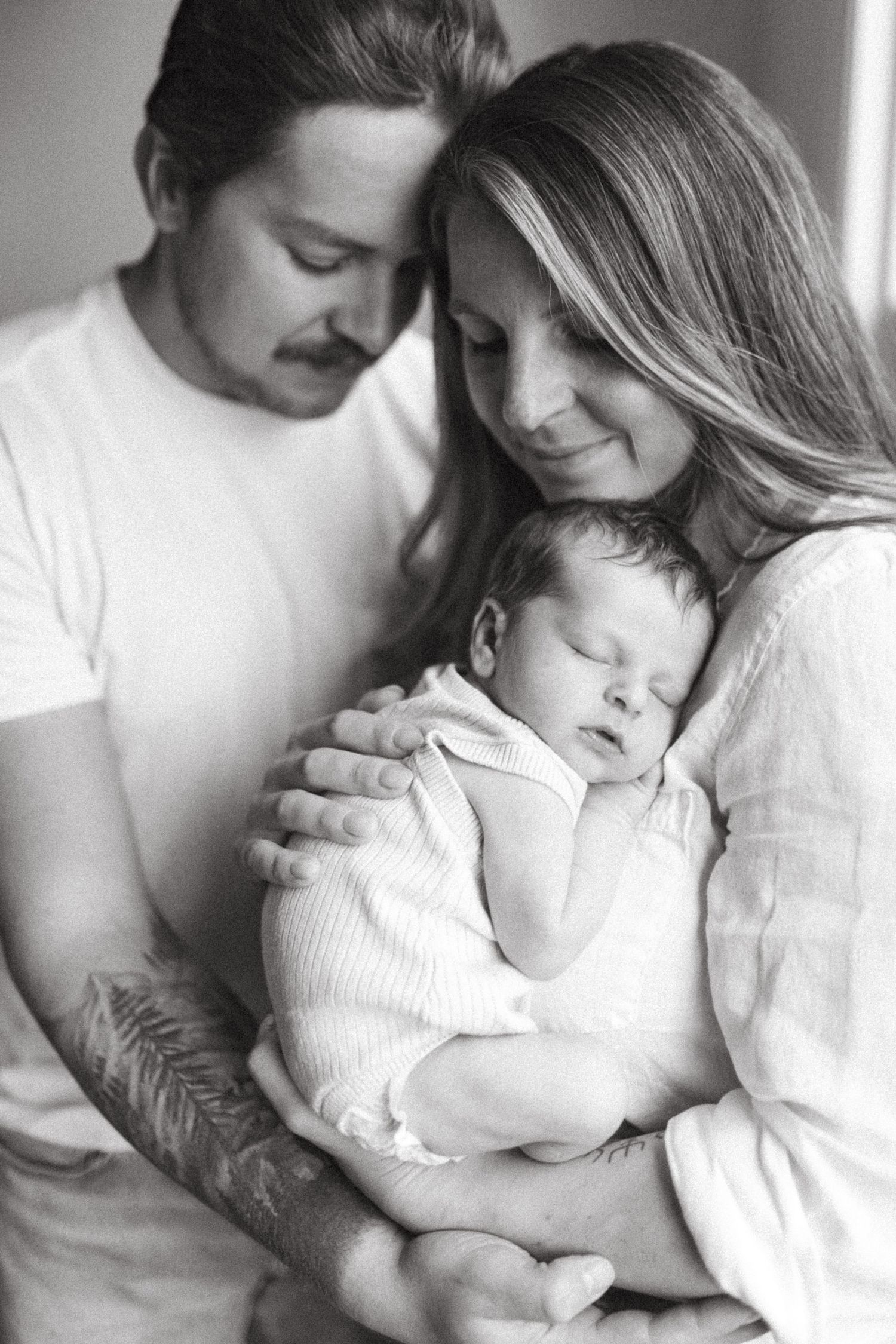 A series of intimate black and white newborn photographs showing tender moments between a couple in white clothing in 100 Mile, BC