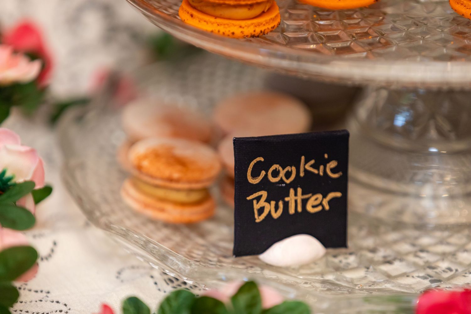Orange and pink macarons arranged on crystal cake stands with black label tags.