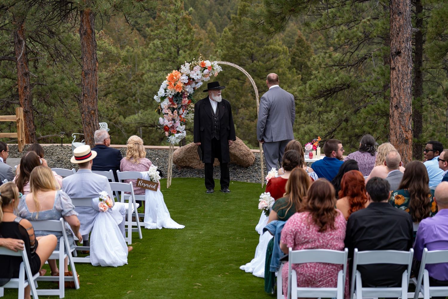 Outdoor wedding ceremony setup with white chairs and pine trees in the background.