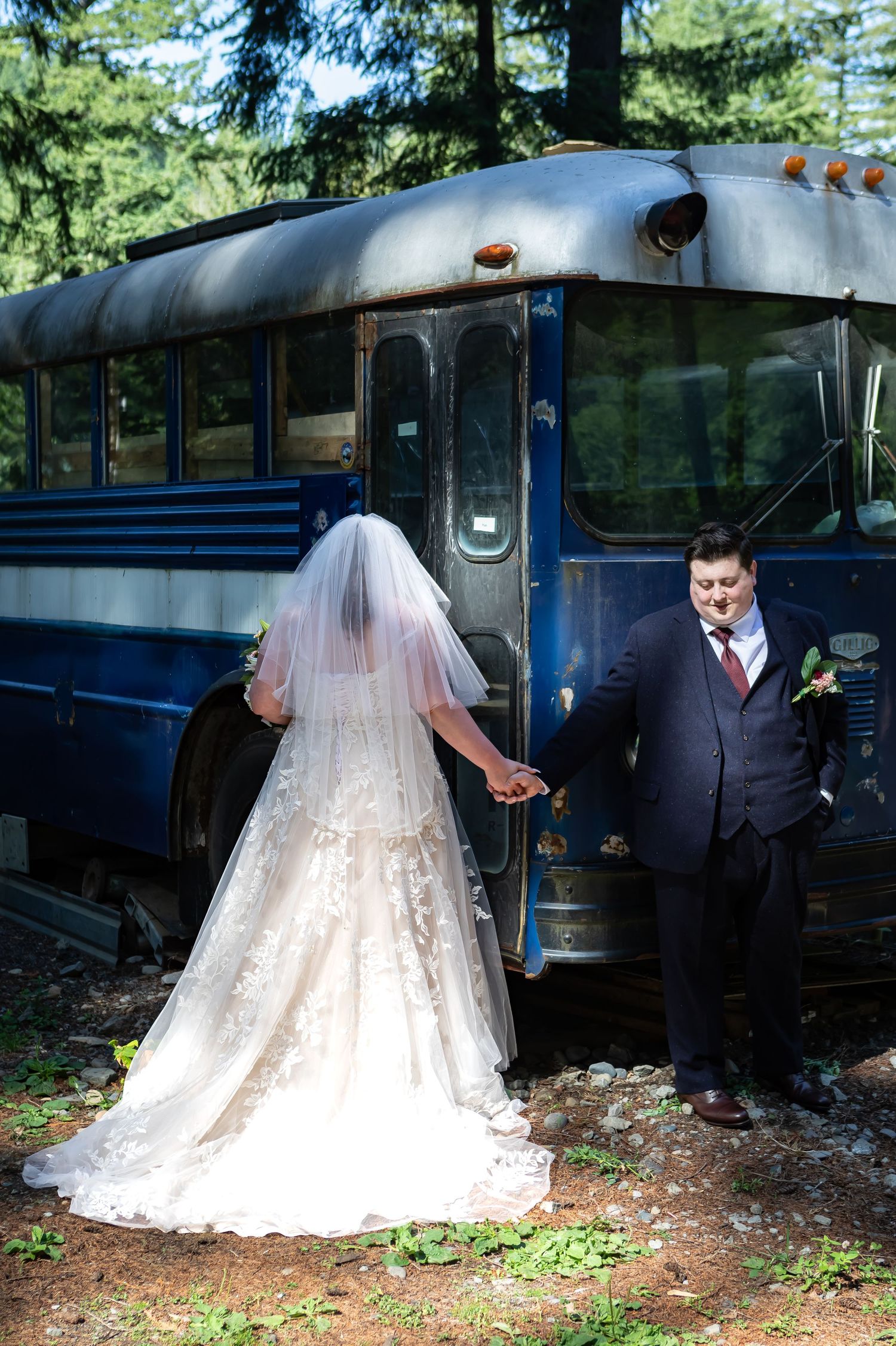 A romantic wedding photo shoot against a vintage blue bus in a forested setting.