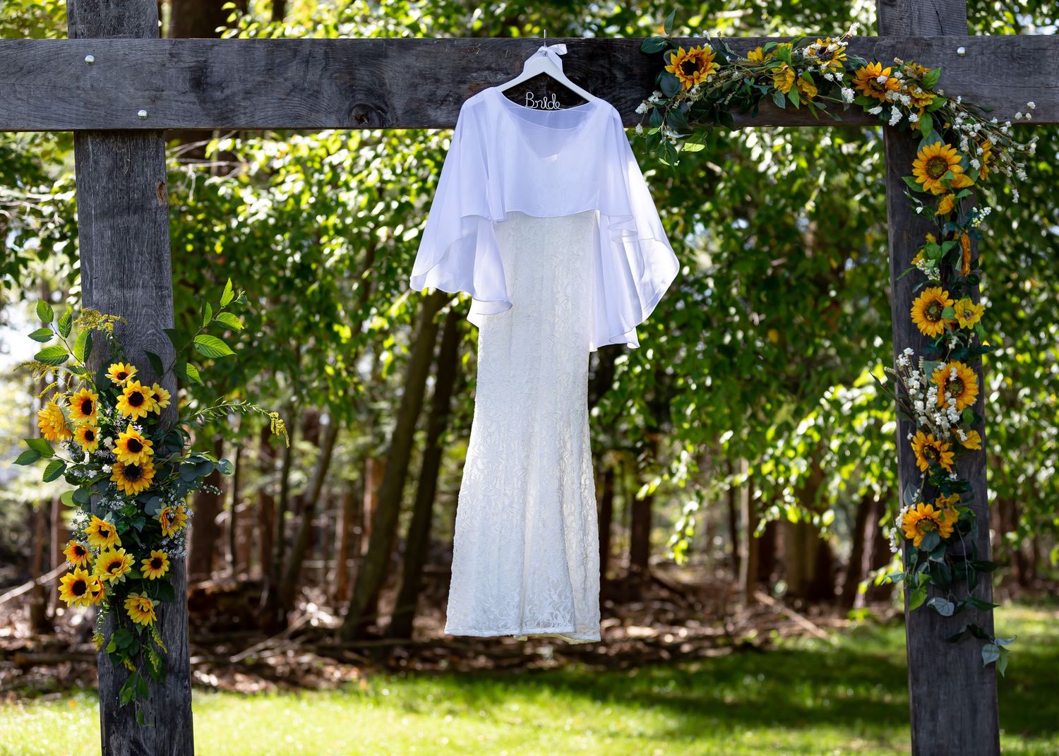 White wedding dress hanging on wooden fence with yellow flowers in garden setting.
