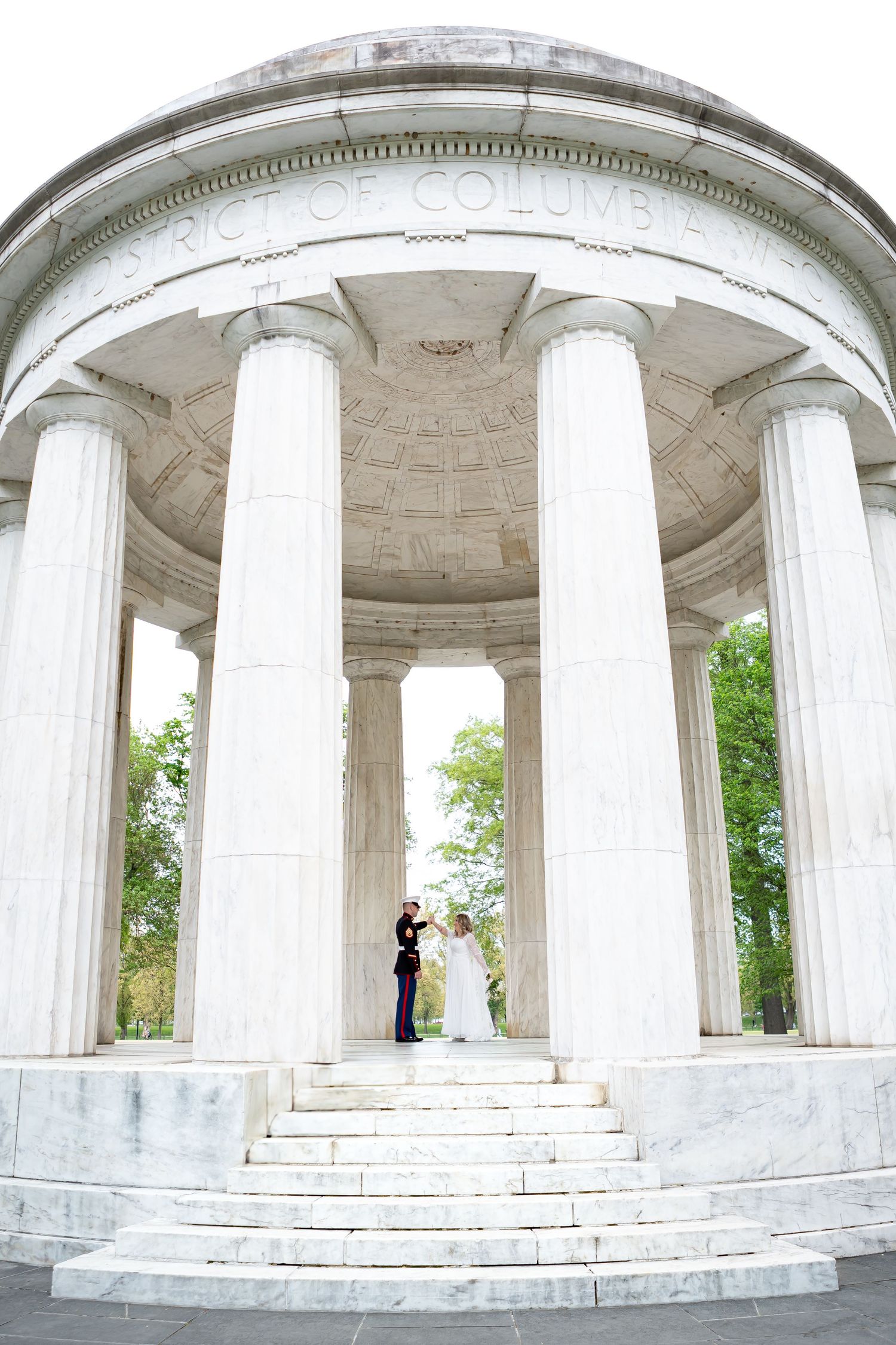 Wedding couple photographed in a classical marble colonnade with white pillars.