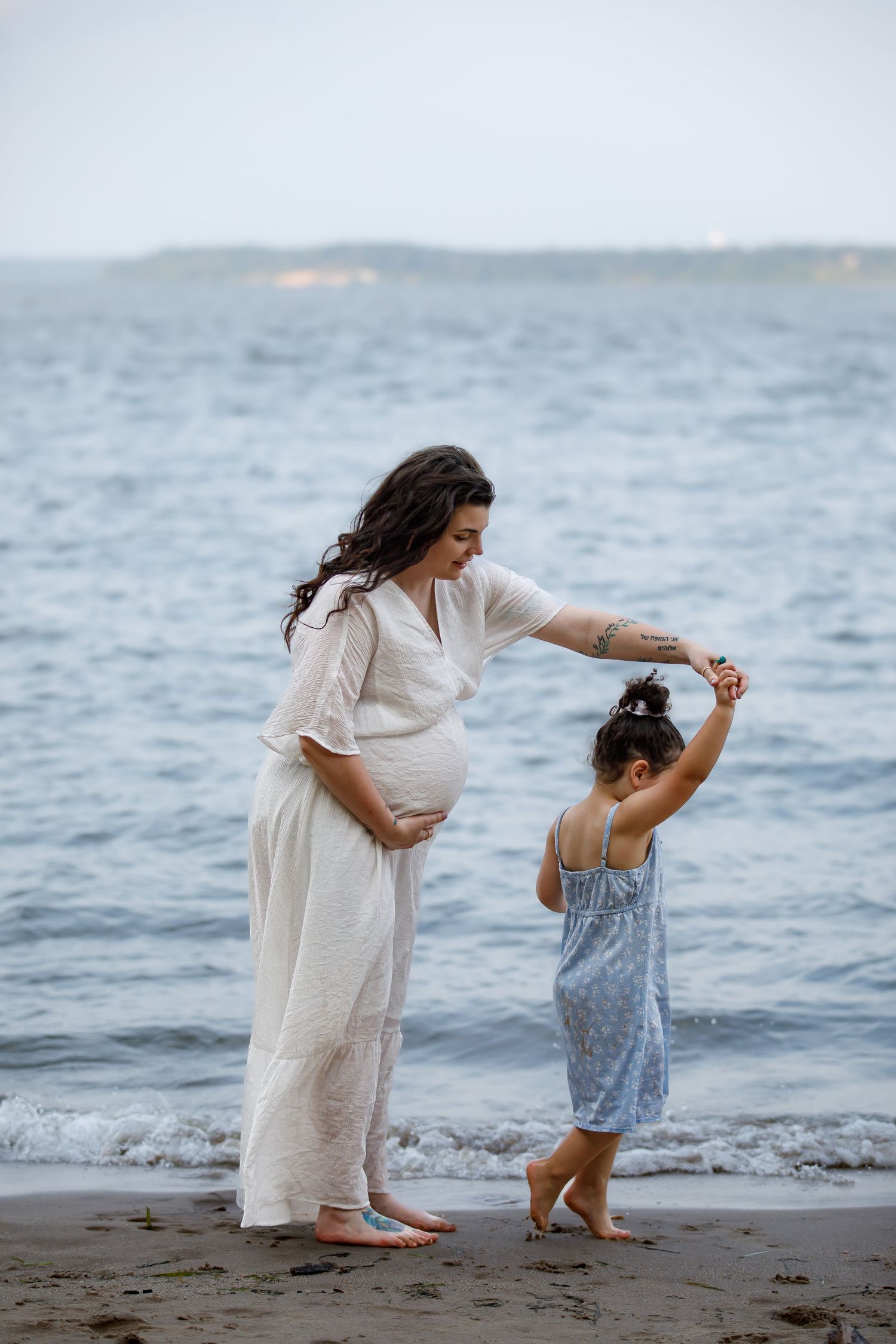 Parent and child dance together on the beach, waves rolling in behind them.
