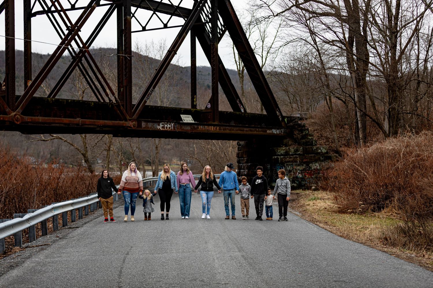 Large family group lined up underneath an old railroad bridge for a wide panoramic shot during a fall family mini session.