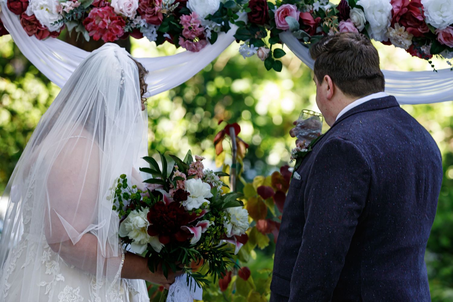 Outdoor wedding ceremony with mauve and green bridesmaid dresses under natural light.