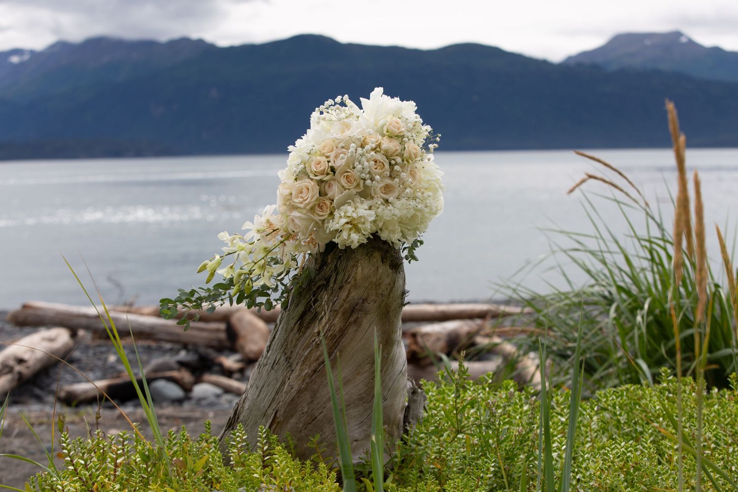 White floral arrangements line a rocky coastal shore with mountains and water in the background.