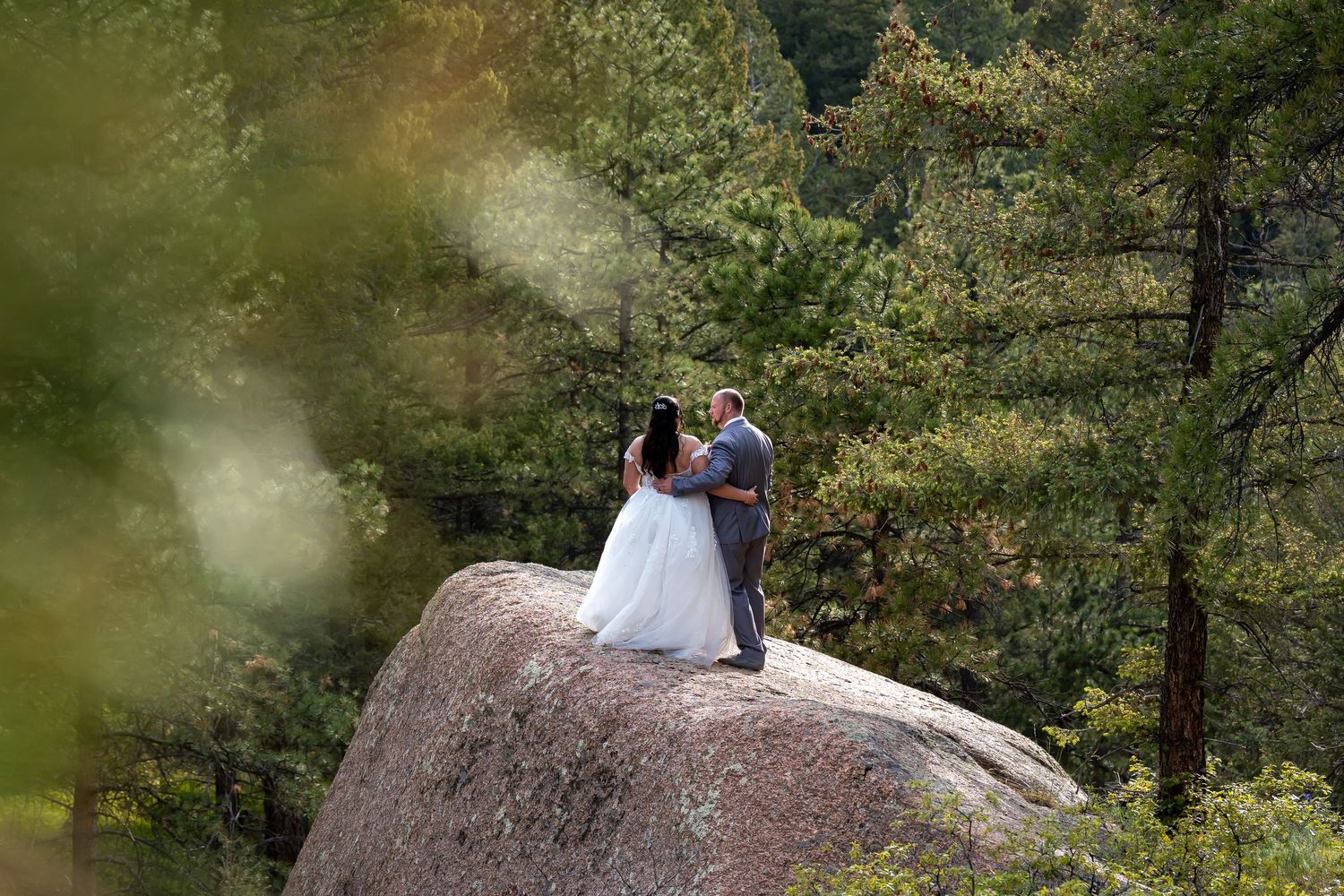 A scenic mountain wedding photoshoot on a large boulder surrounded by evergreen forest.