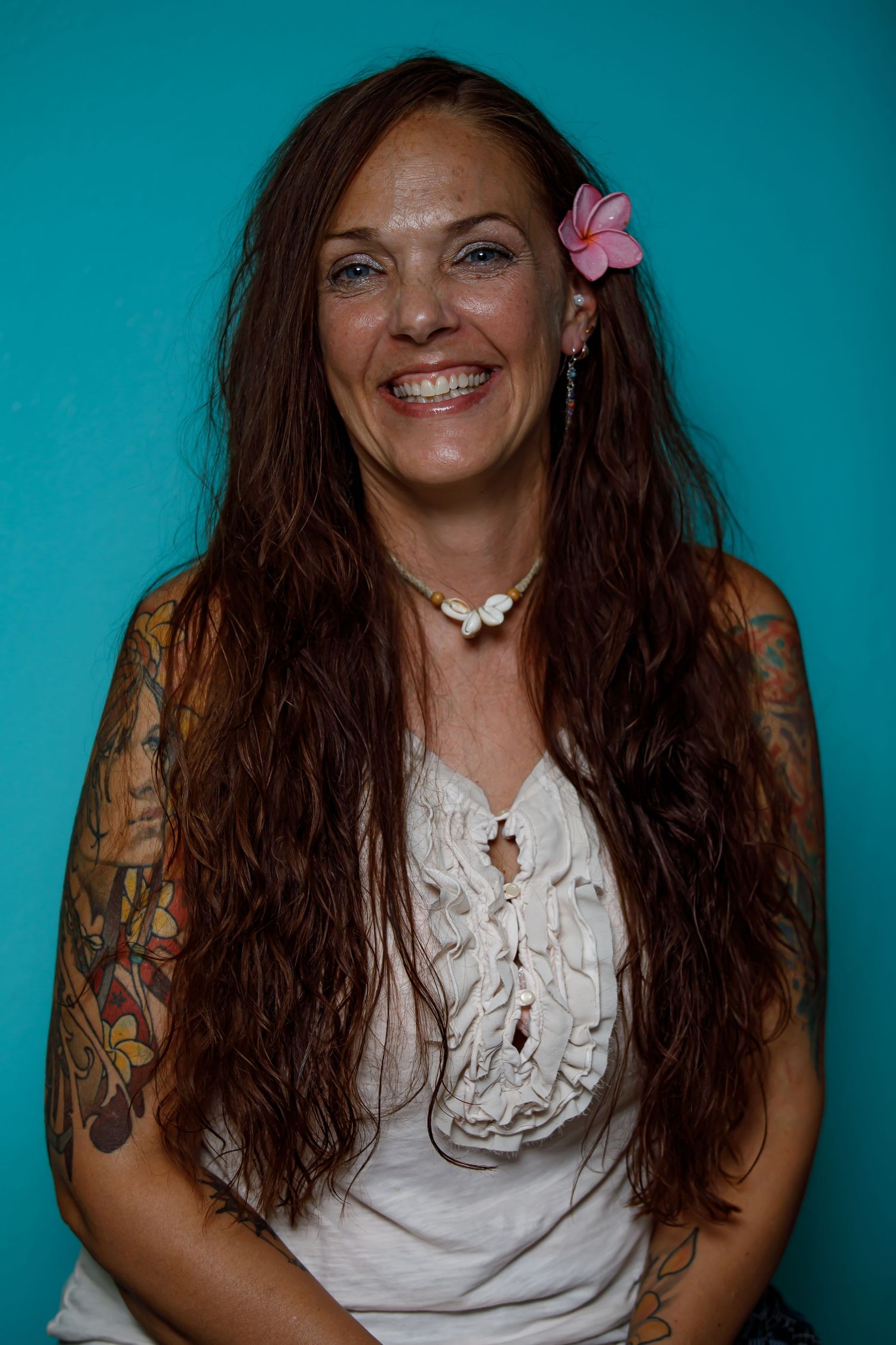 Portrait against turquoise background showing white lace top and floral accessories.