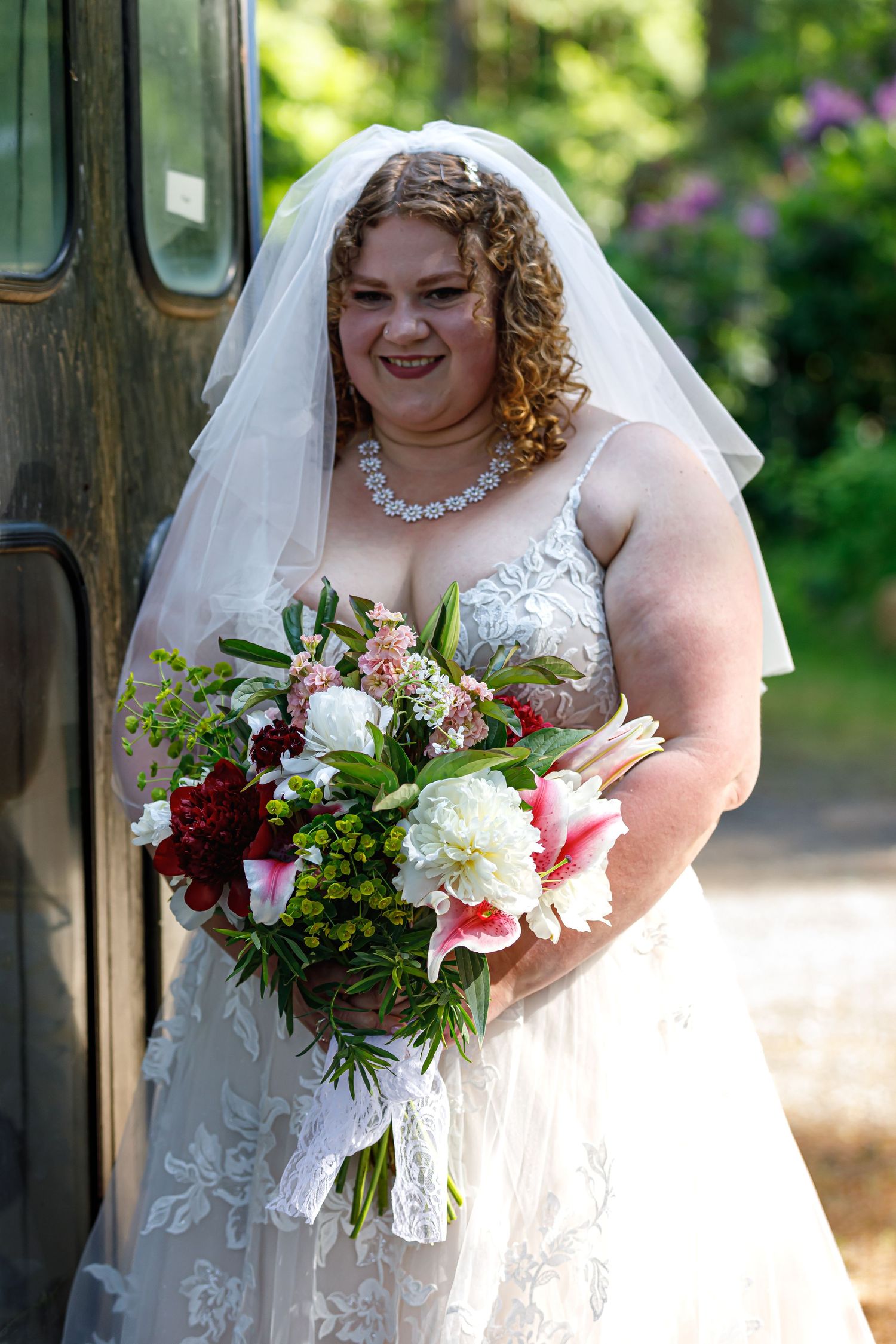 A bridal portrait showcasing a beautiful bouquet with white and red flowers in natural sunlight.