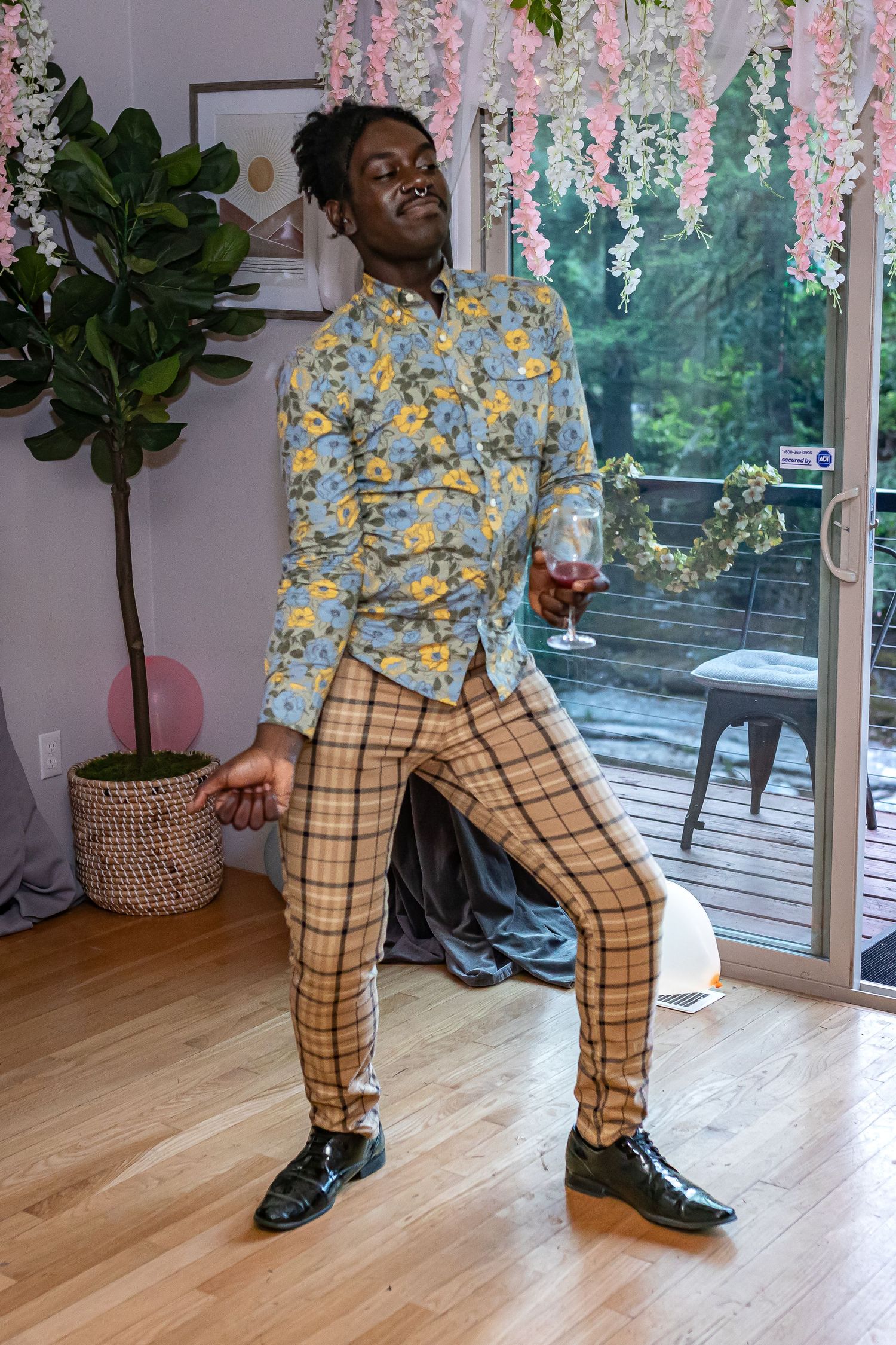 Person dancing in plaid pants and floral shirt under pink and teal decorative lighting.
