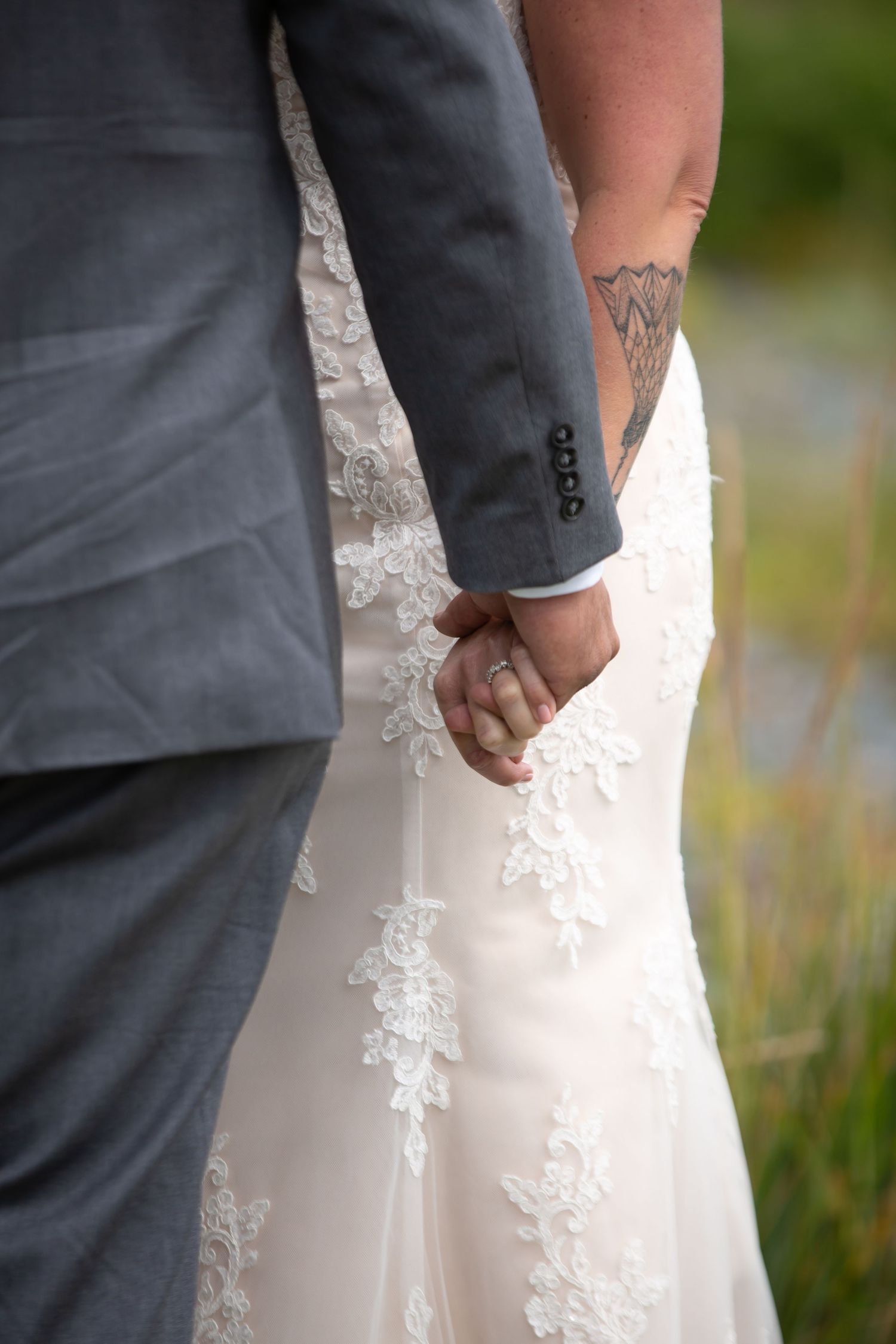 Close-up of couple holding hands showing tattoo and lace wedding dress details.