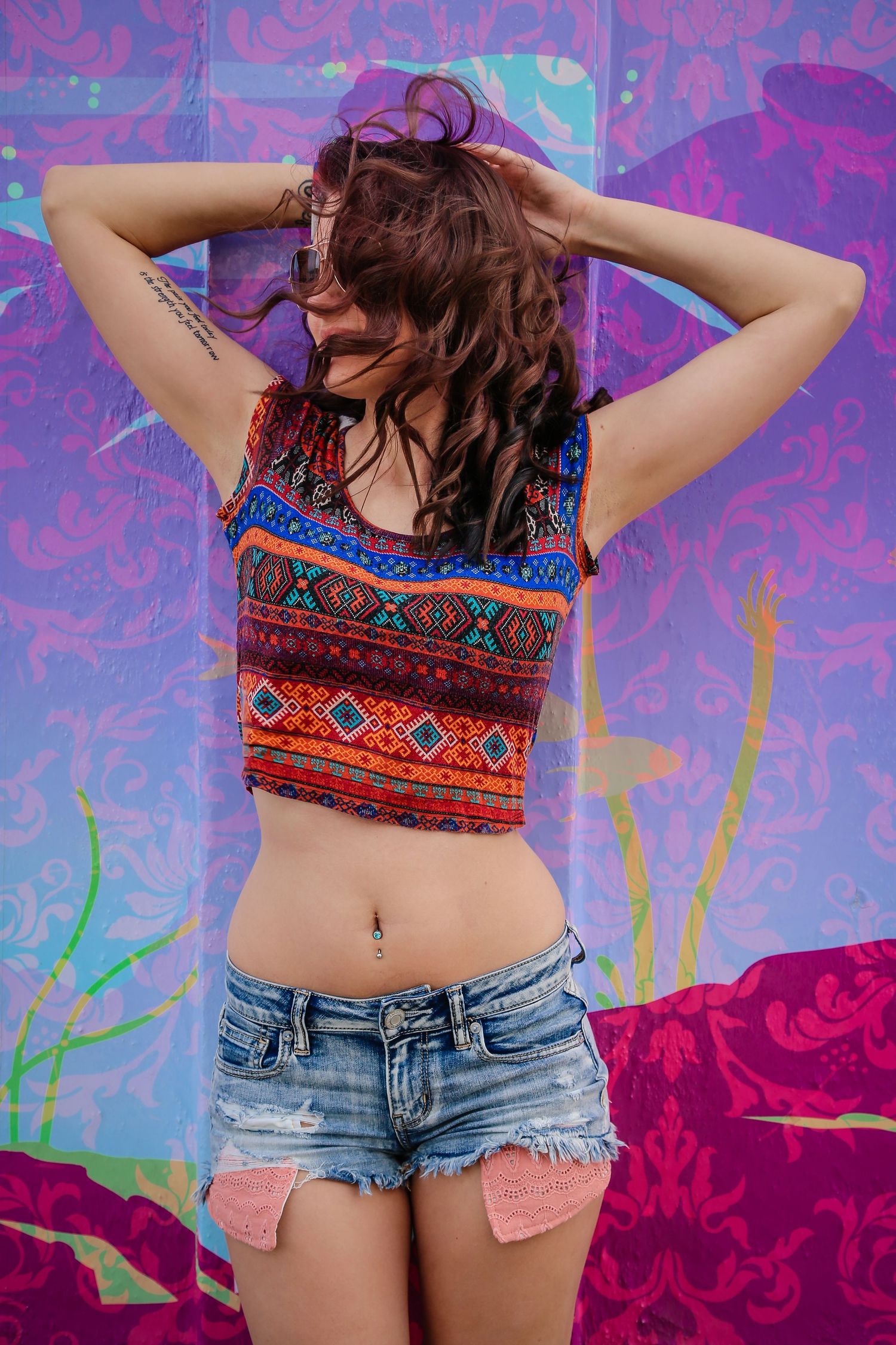 A colorful fashion photo against vibrant purple and pink graffiti wall featuring denim shorts and patterned crop top.