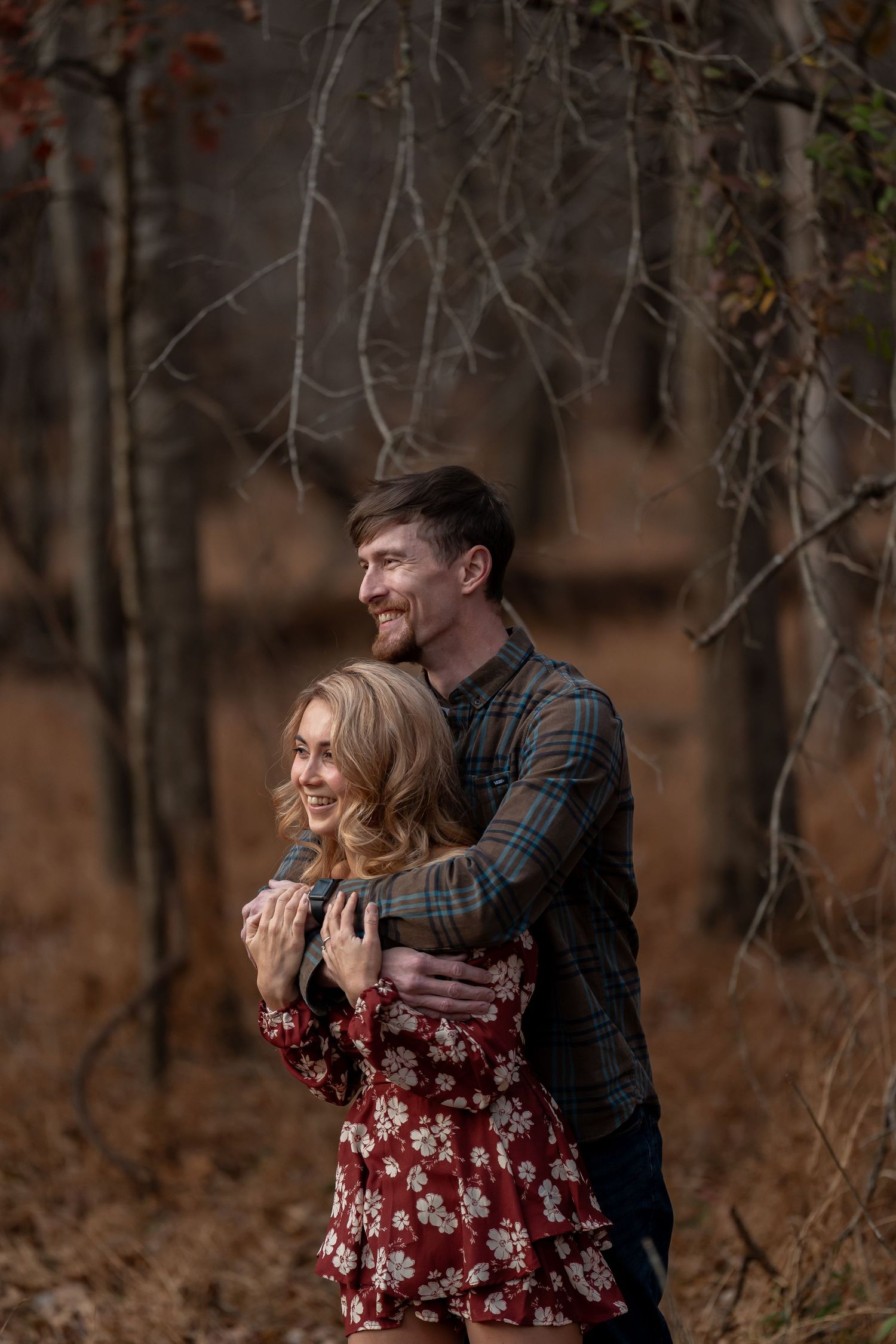 A couple embraces and laughs together in a wooded area during fall.