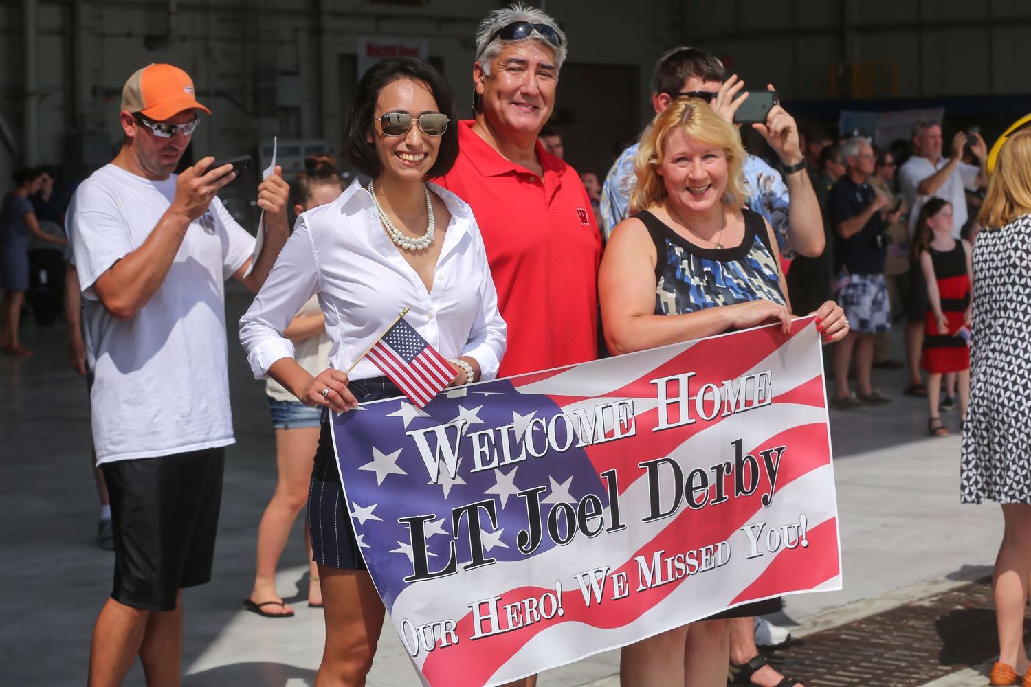 Crowd holds welcome home banners and American flags at military homecoming event.