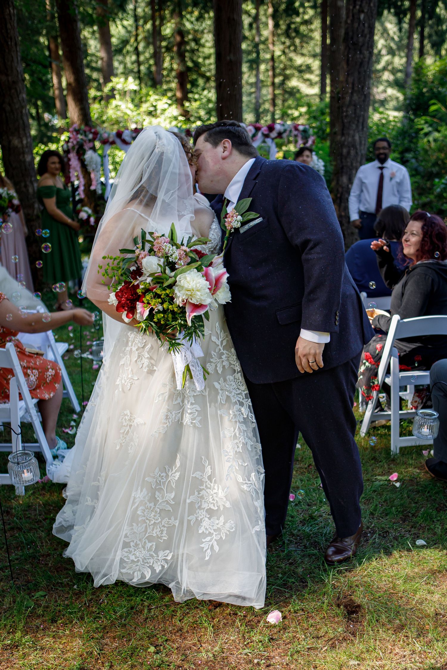 Wedding ceremony procession in a natural wooded setting with white chairs.