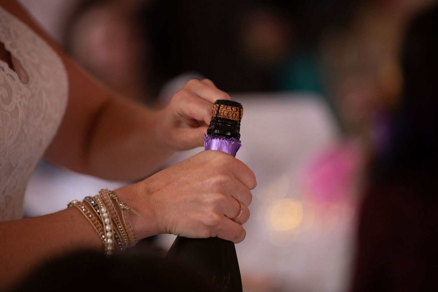 Close-up of hands holding wine bottle with gold bracelet accessory.