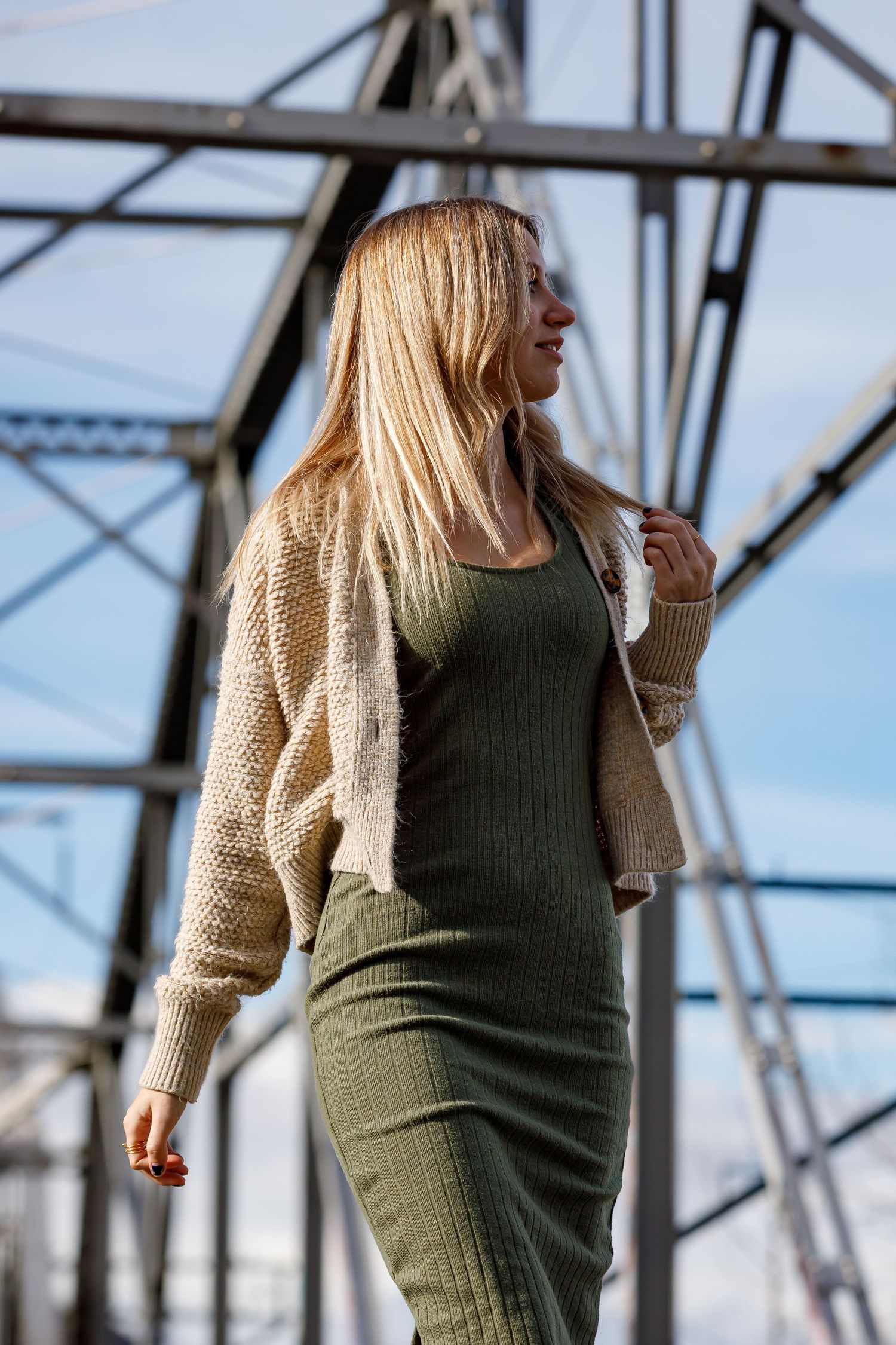 A person in a green top and beige cardigan poses against an industrial metal structure background.
