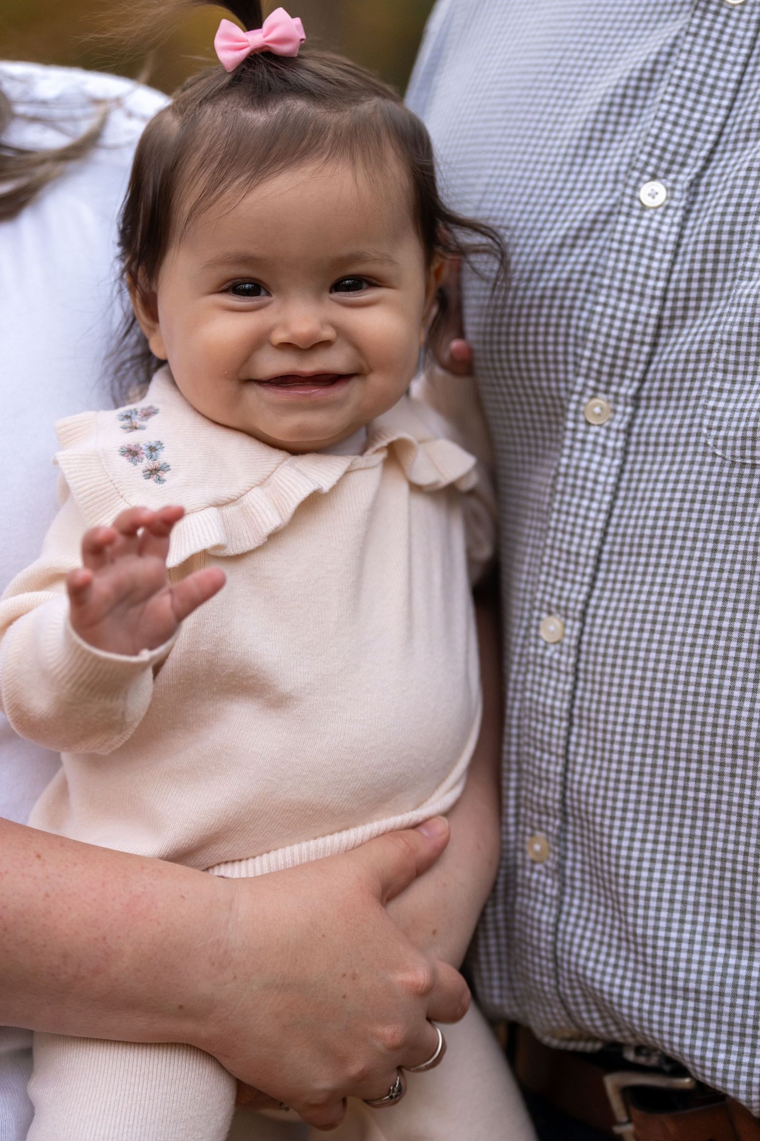 A baby wearing a pink bow and cream-colored outfit smiles at the camera.
