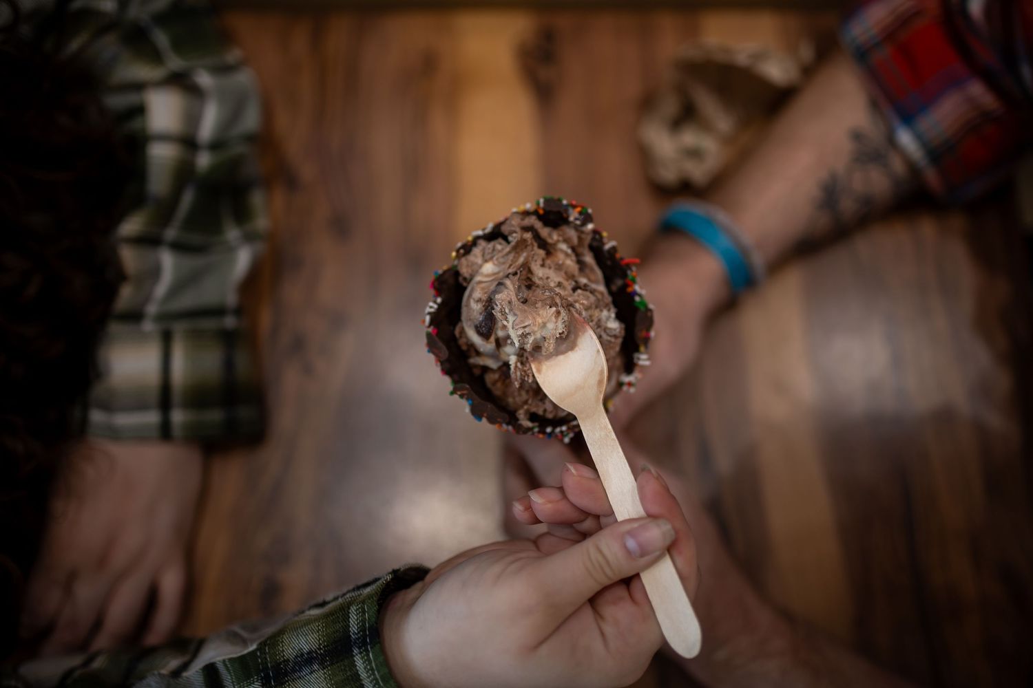 Hand holding chocolate-covered ice cream bar with wooden stick.