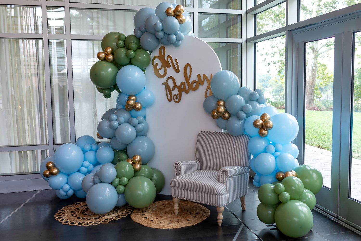 Elegant balloon arch display with blue and green balloons against white walls in an indoor space.