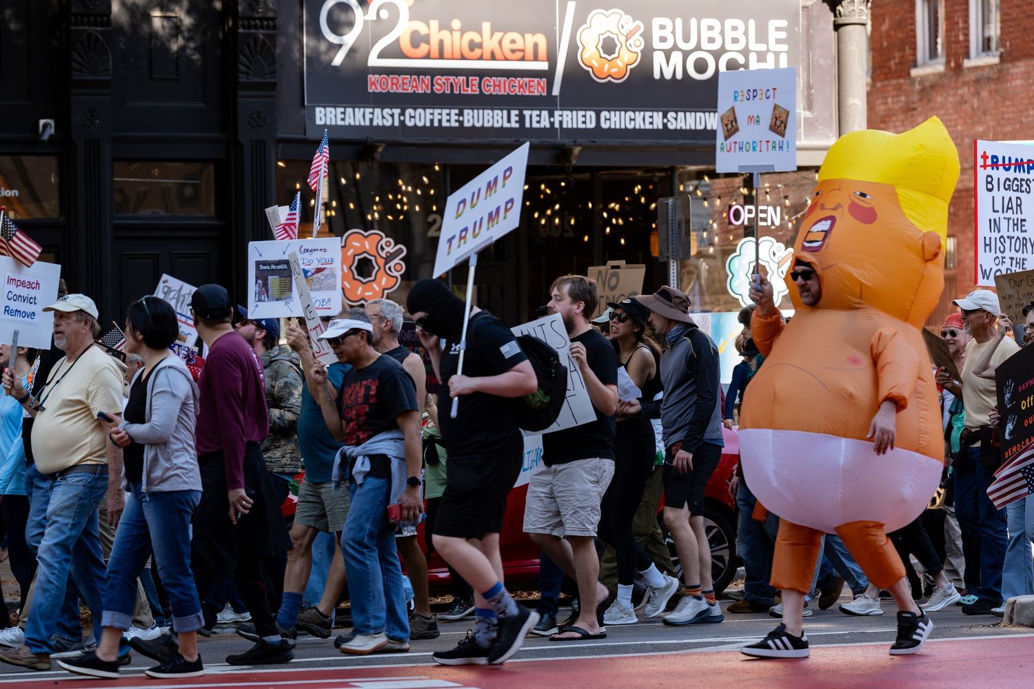 Street protest with inflatable characters and demonstrators holding signs.