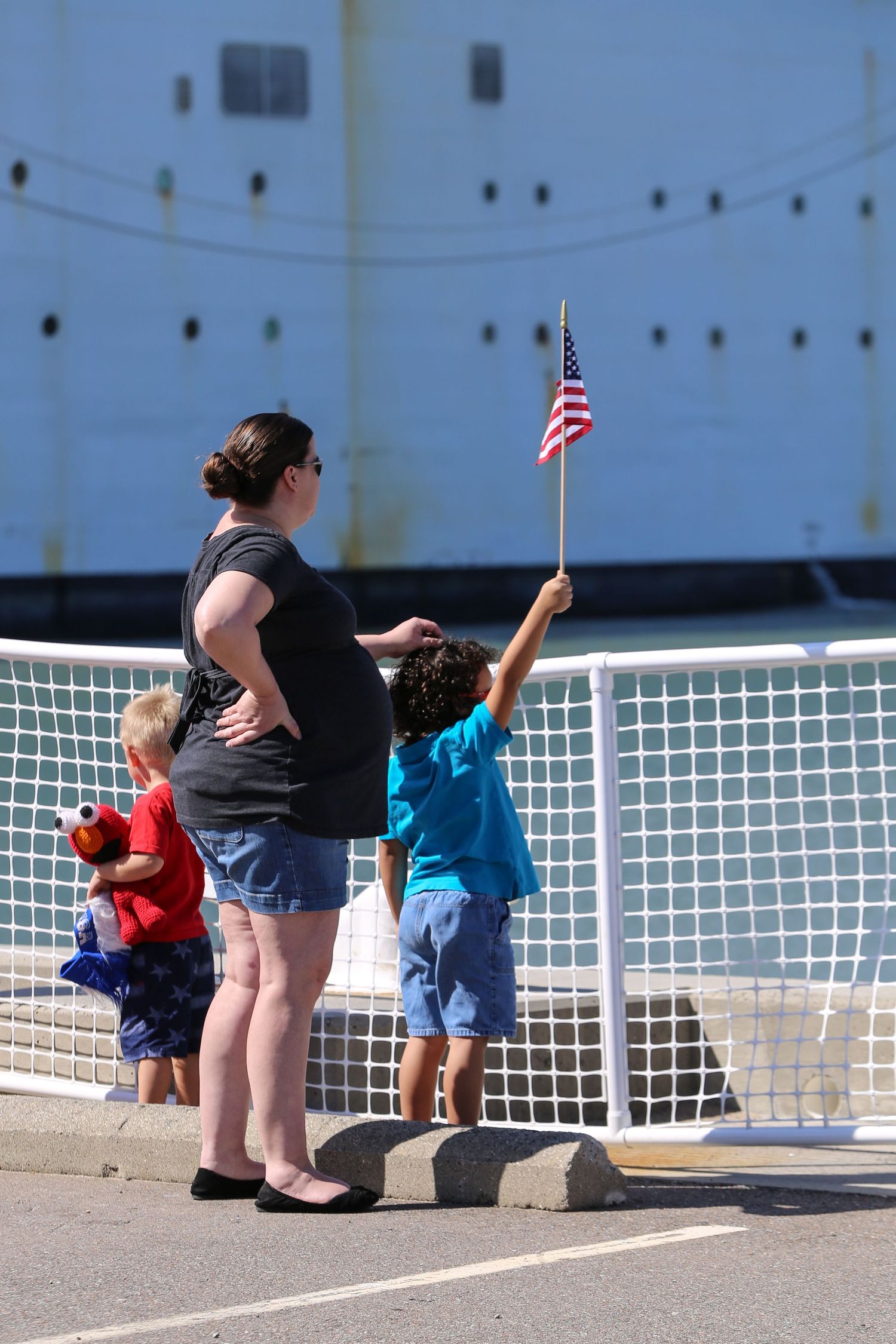 People sitting along a white railing waving small American flags.