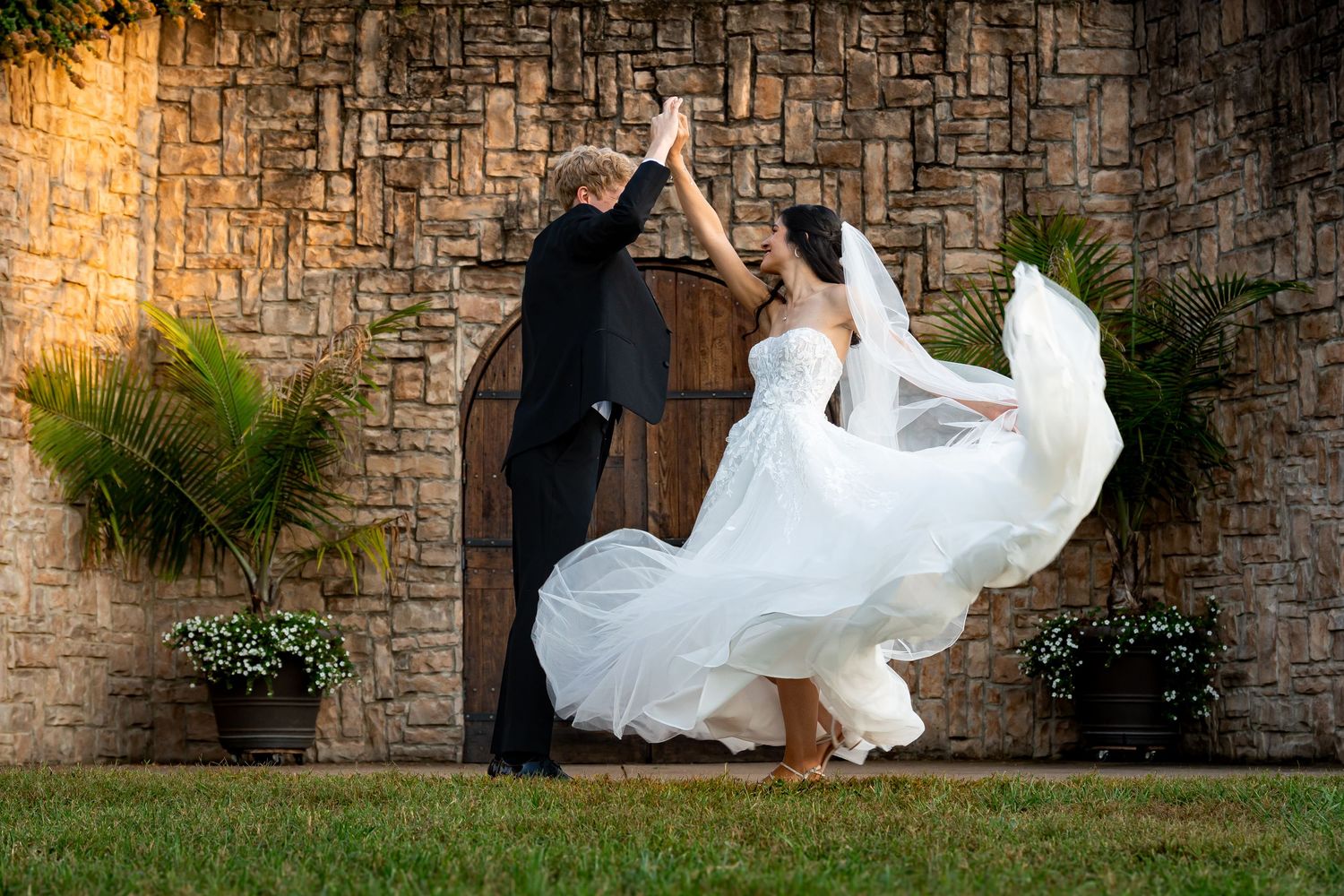 Bride's white dress flows dramatically against textured stone wall during wedding portraits.