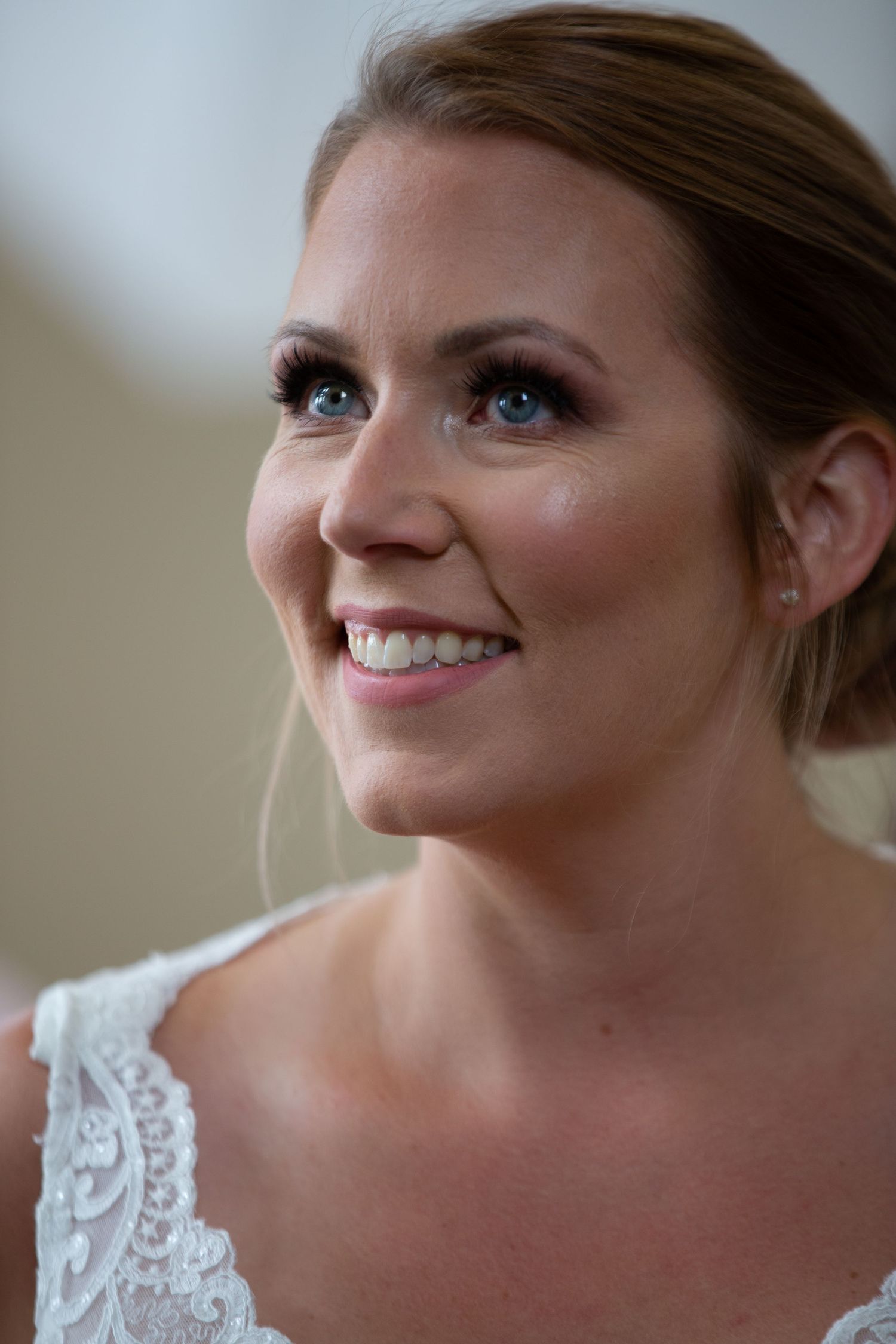Close-up shots of bride in white lace wedding dress smiling joyfully during pre-wedding preparation.