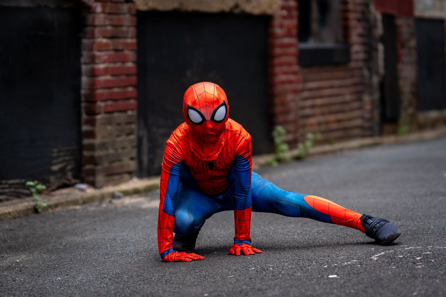 Spider-Man cosplayer in classic red and blue suit posing dramatically on urban street.