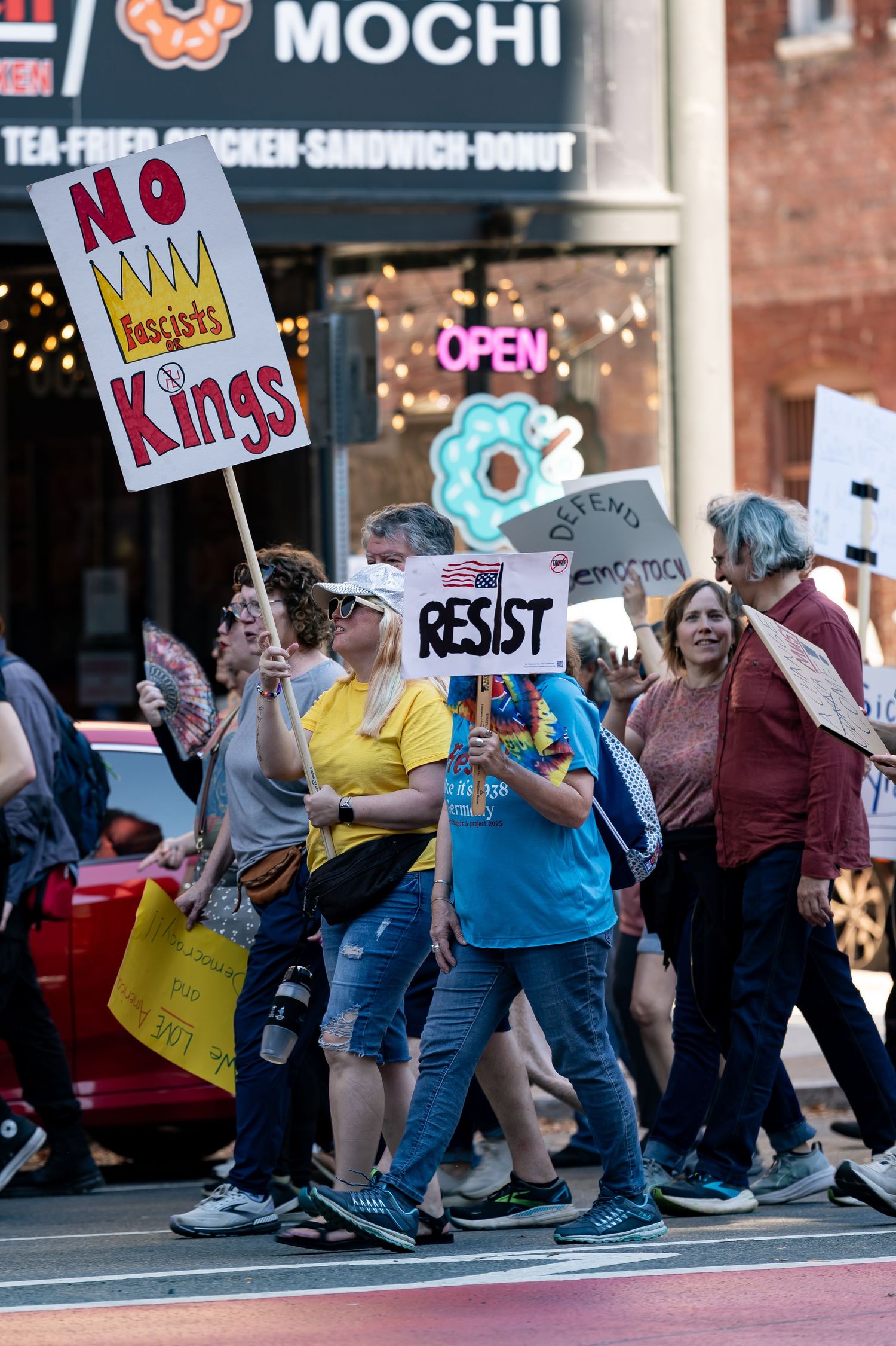 Protesters with signs lined up in front of a Mochi restaurant storefront.