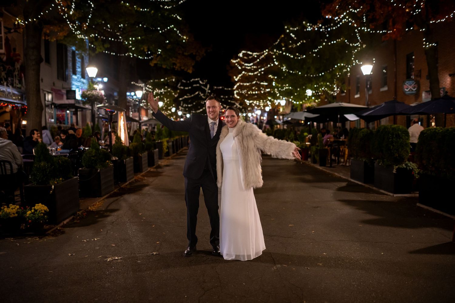 Nighttime wedding photos on city street illuminated by string lights.