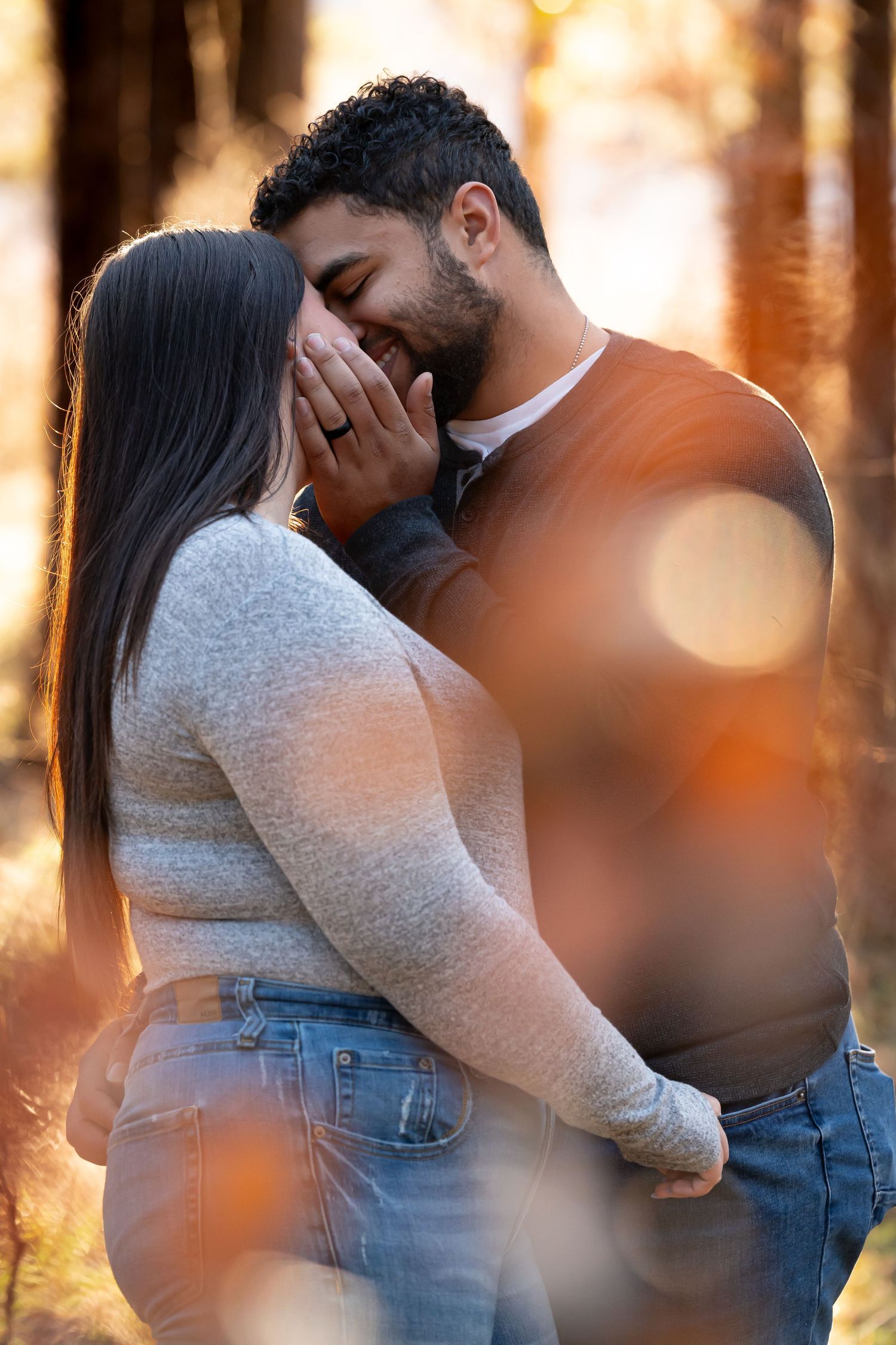Intimate couple sharing a tender moment in autumn forest with golden bokeh light effects in background.