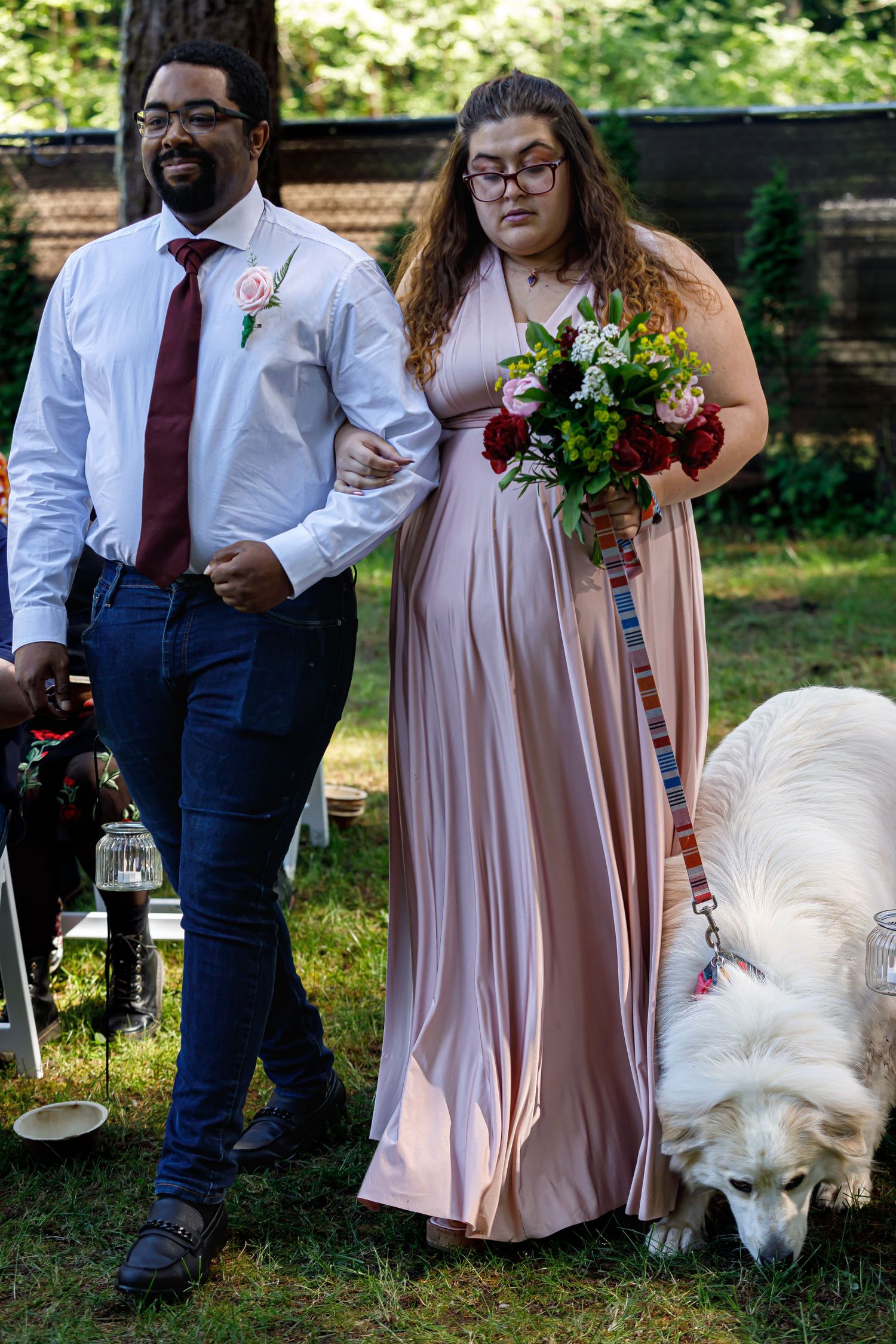 Wedding party in pink dresses and burgundy ties gathering for outdoor garden photos.