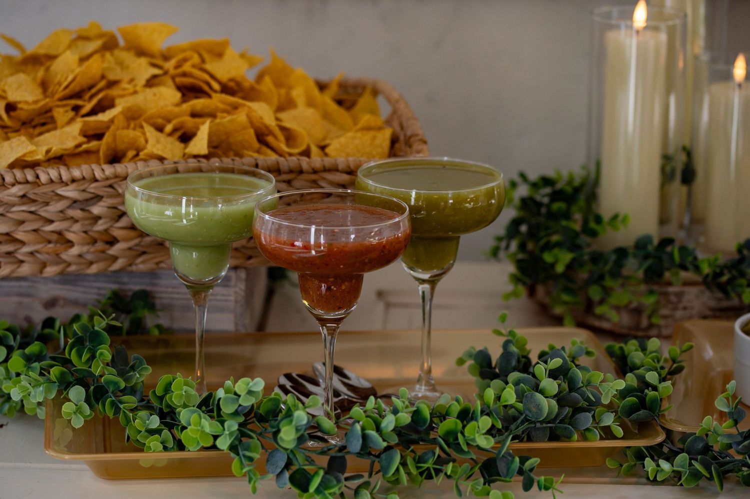 Colorful cocktails in martini glasses displayed with tortilla chips and greenery decorations.