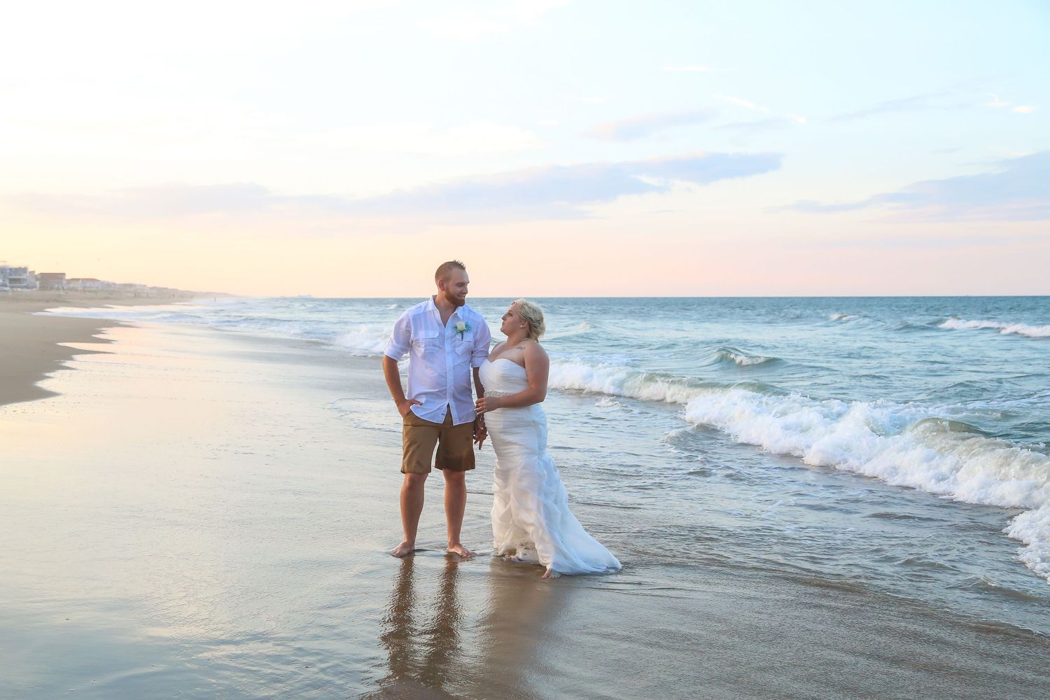 Couple walking along beach shoreline at sunset in wedding attire.