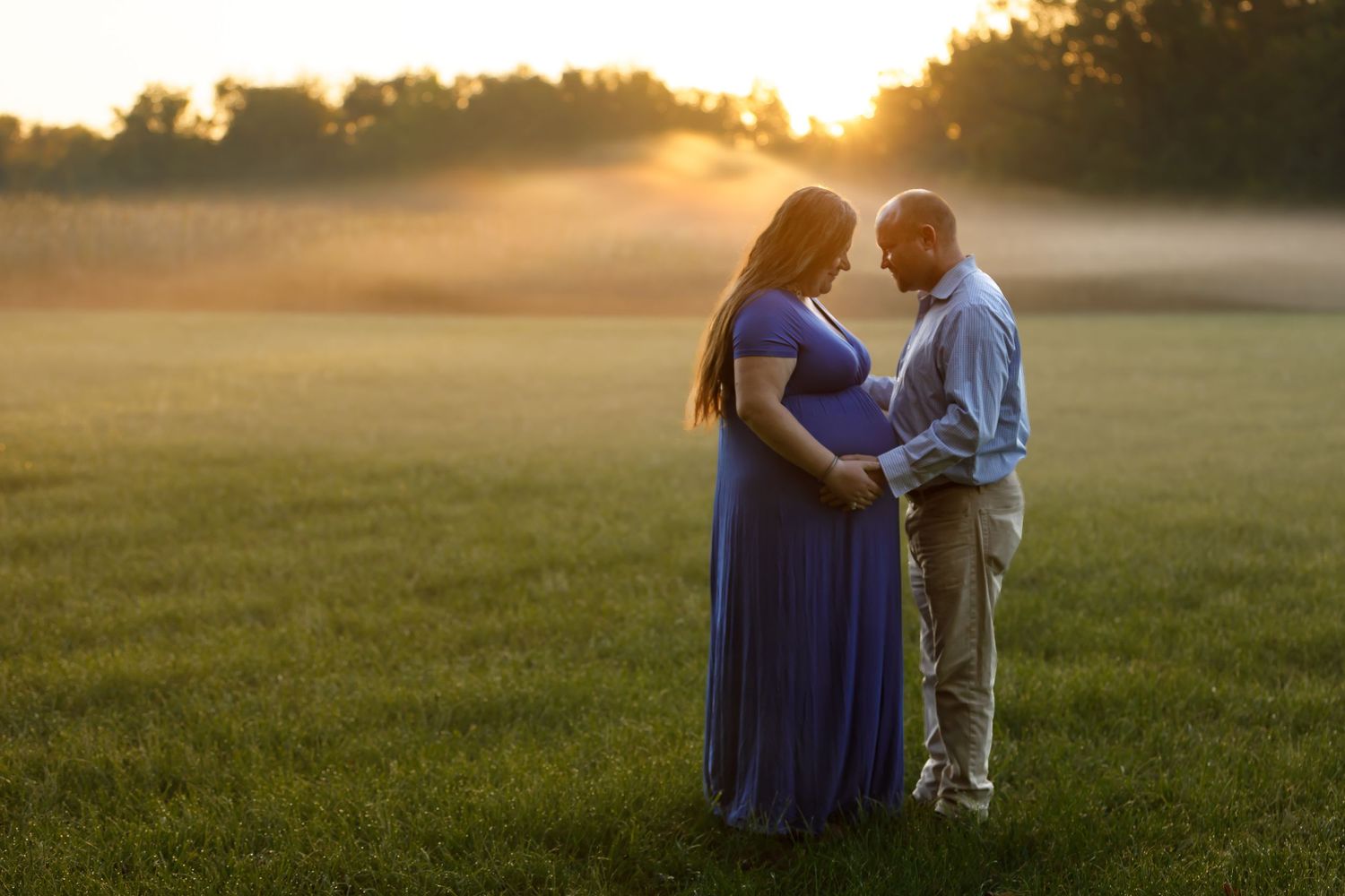 A couple shares an intimate moment in a misty field during sunset.