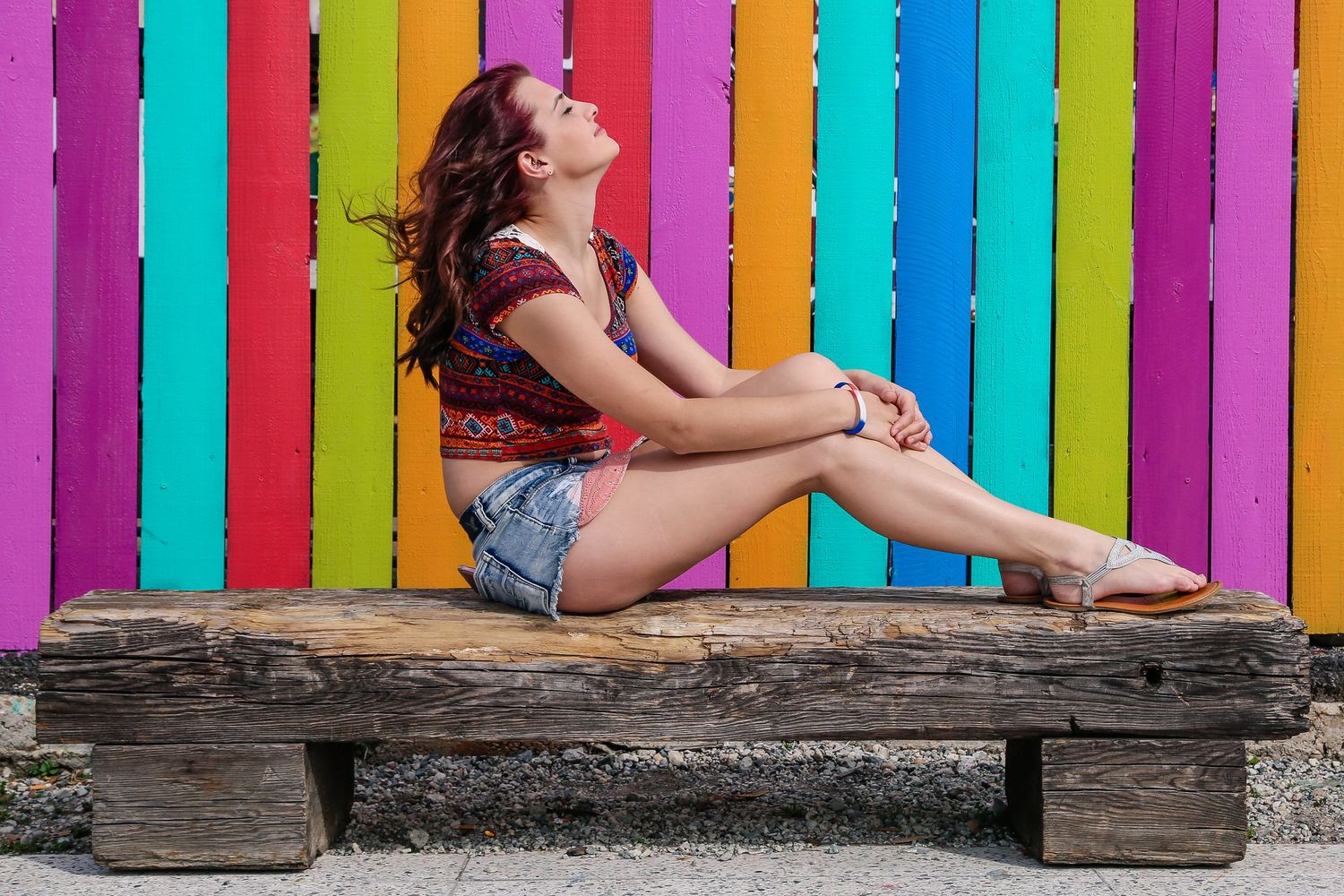 Model poses in front of a rainbow striped wall with wooden bench.