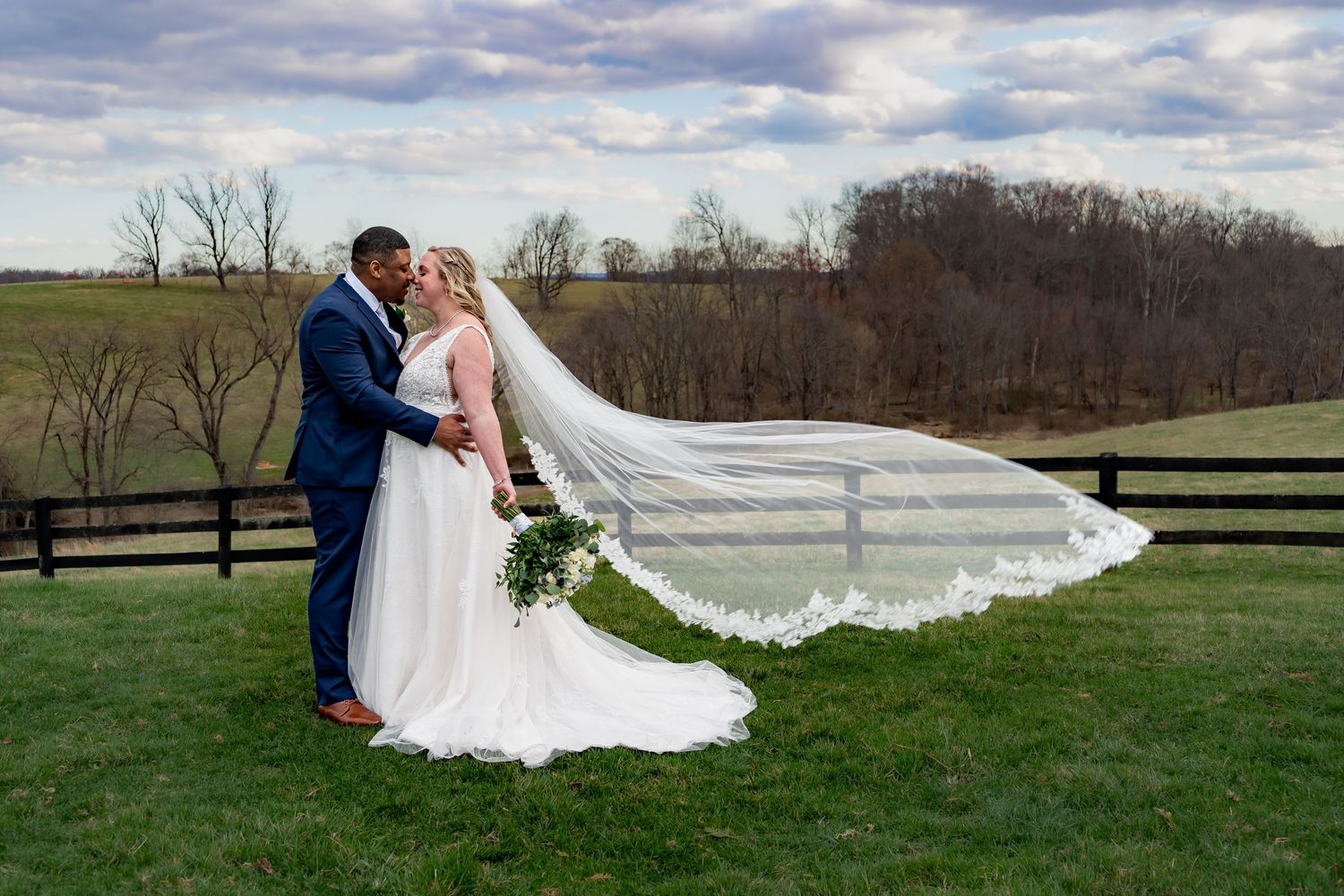 A wedding couple poses in a green field with dramatic clouds overhead.