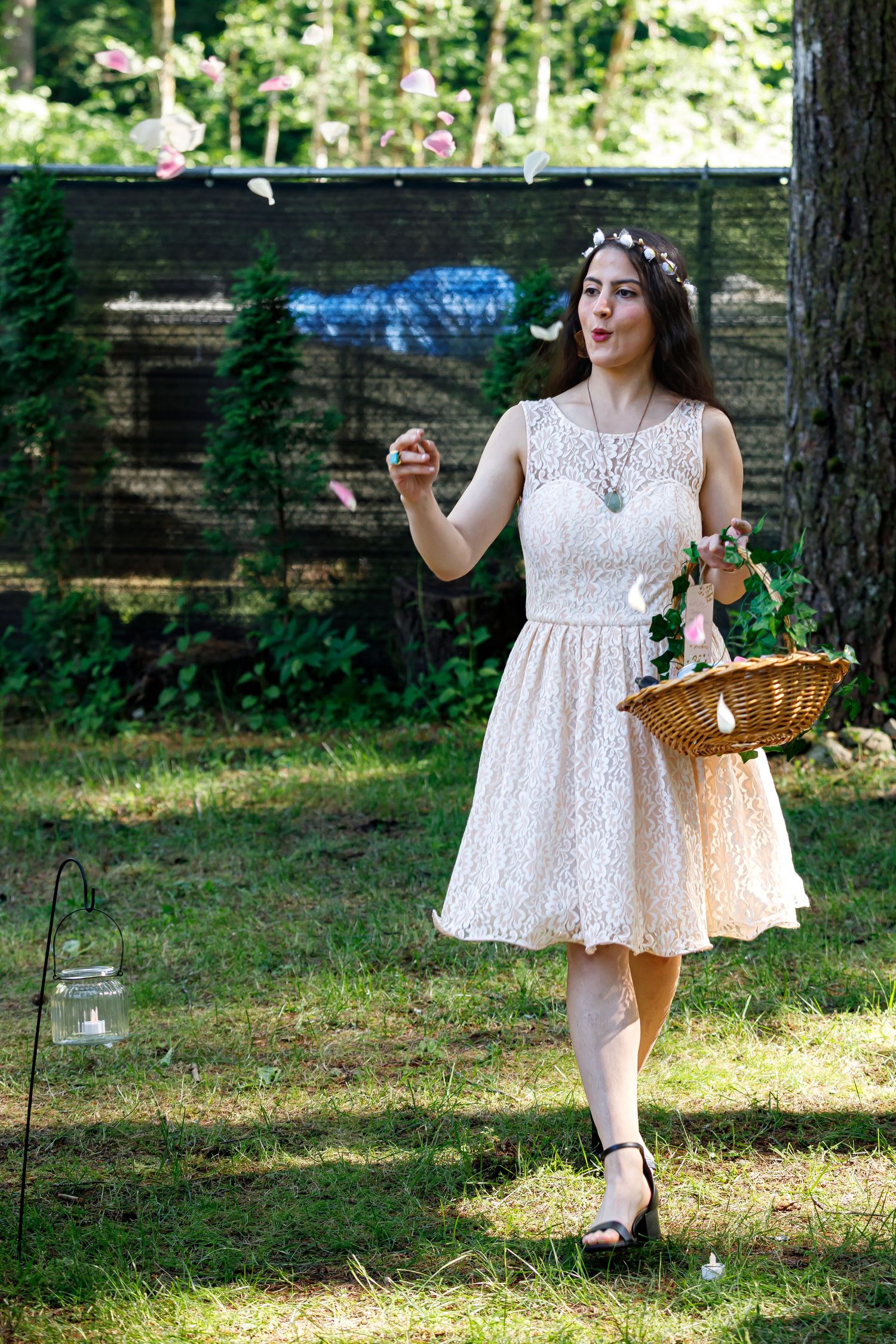A person in a white lace dress twirls playfully in a sunlit garden while holding a wicker basket.