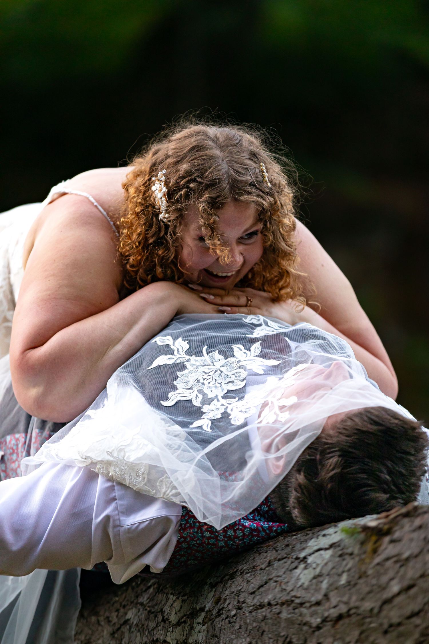 A couple shares an intimate moment while lying on a large tree trunk outdoors.