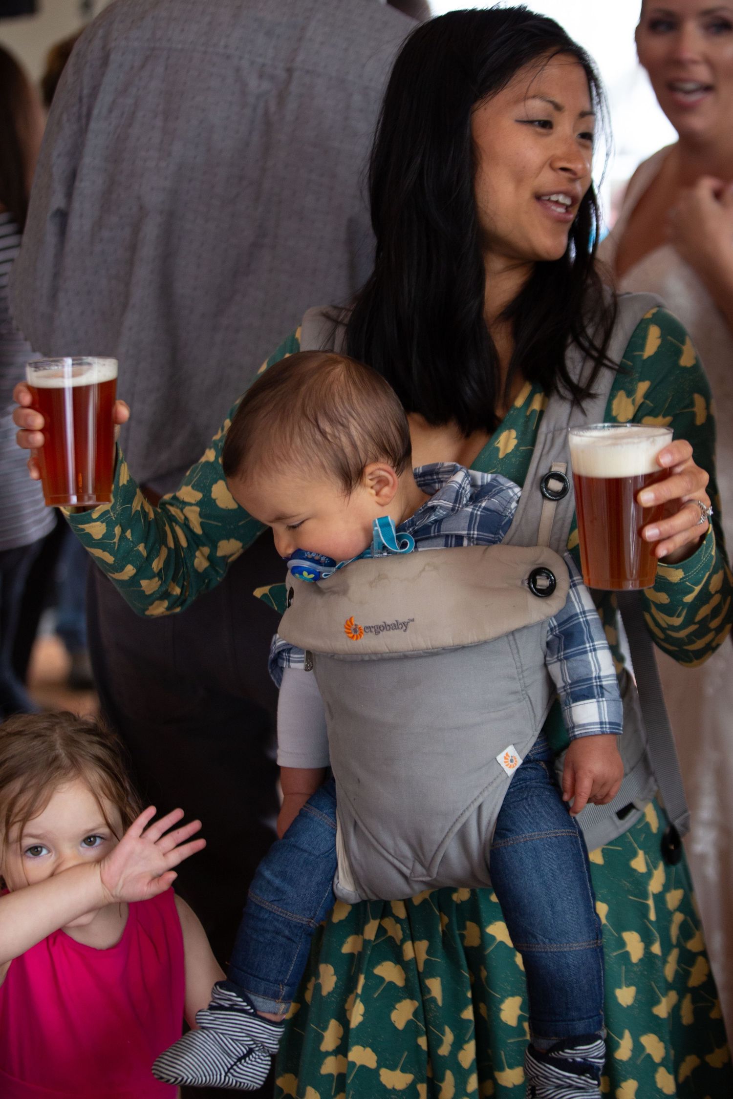 Family gathering with baby carrier and drinks at a social celebration.
