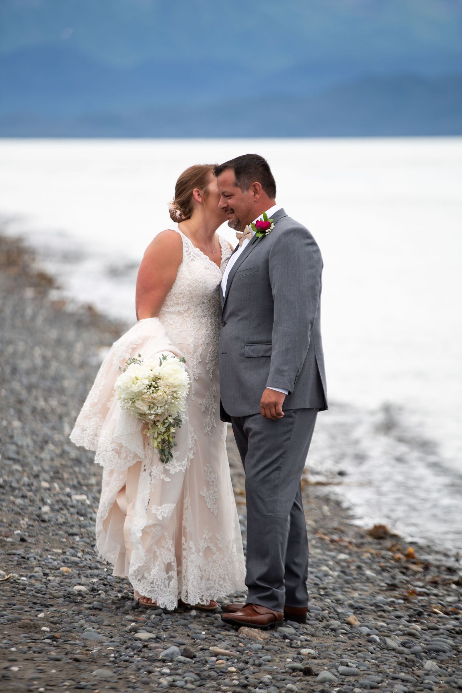 A romantic moment between newlyweds on a pebble beach with white bouquet.