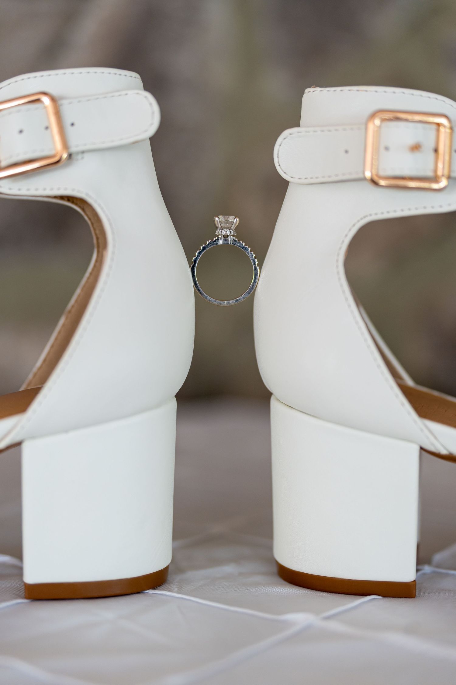 White wedding shoes with rose gold buckles frame an elegant engagement ring.