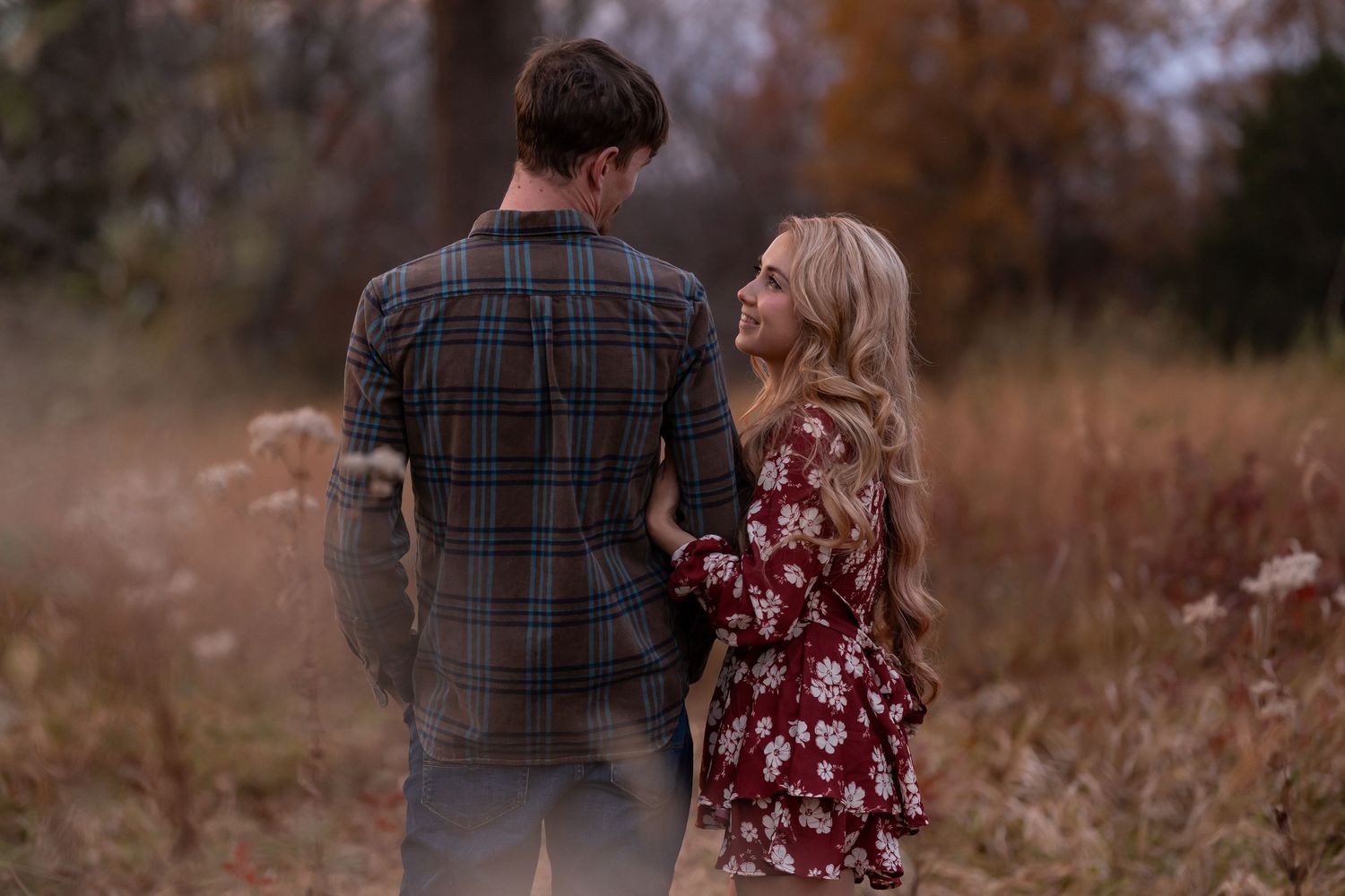 A couple in casual attire shares an intimate moment against a backdrop of fall trees.