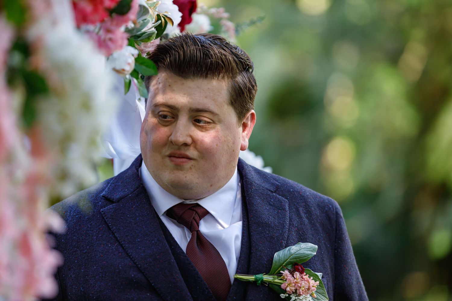 Wedding party members in formal attire and burgundy accessories pose for outdoor portraits.